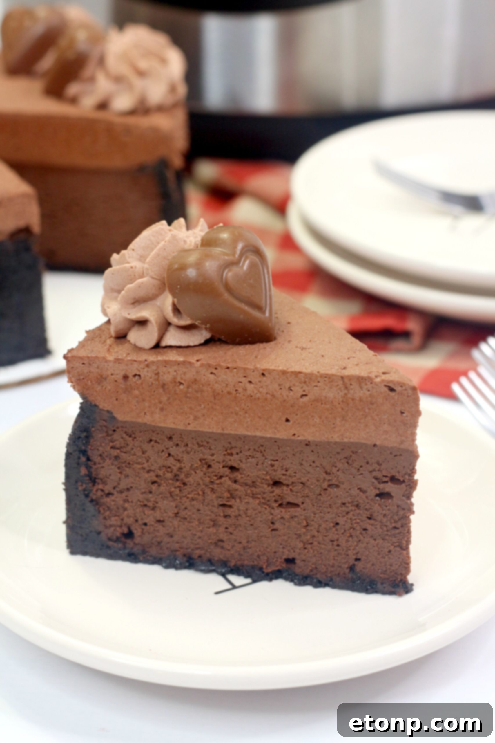 A single slice of Triple Chocolate Godiva Cheesecake on a white plate, garnished with chocolate hearts and whipped cream