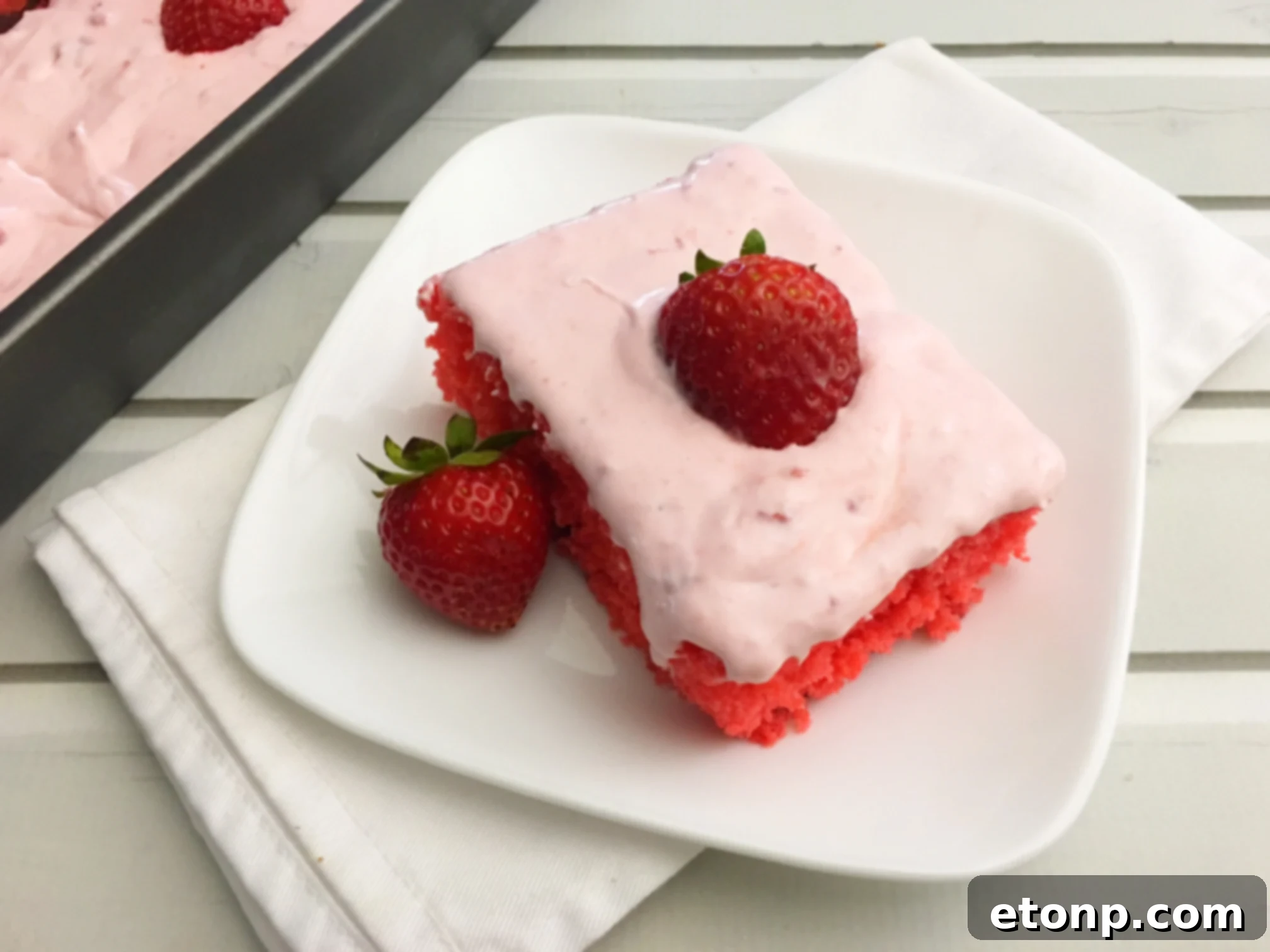 Another close-up of the Strawberry Jello Cake, highlighting the rich frosting and fresh strawberry garnishes, ready to be enjoyed.