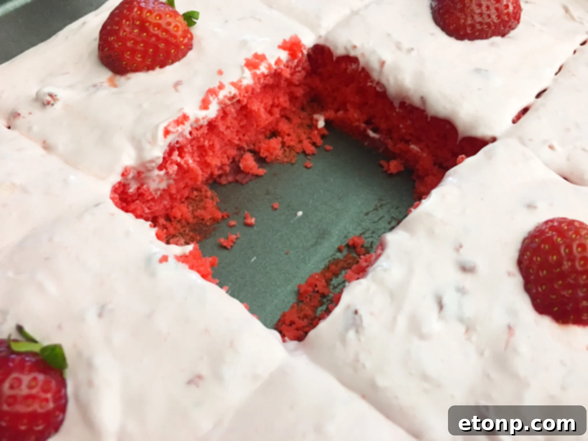 A frosted Strawberry Jello Cake, seen from an angle, with a generous layer of buttercream and fresh strawberry slices.
