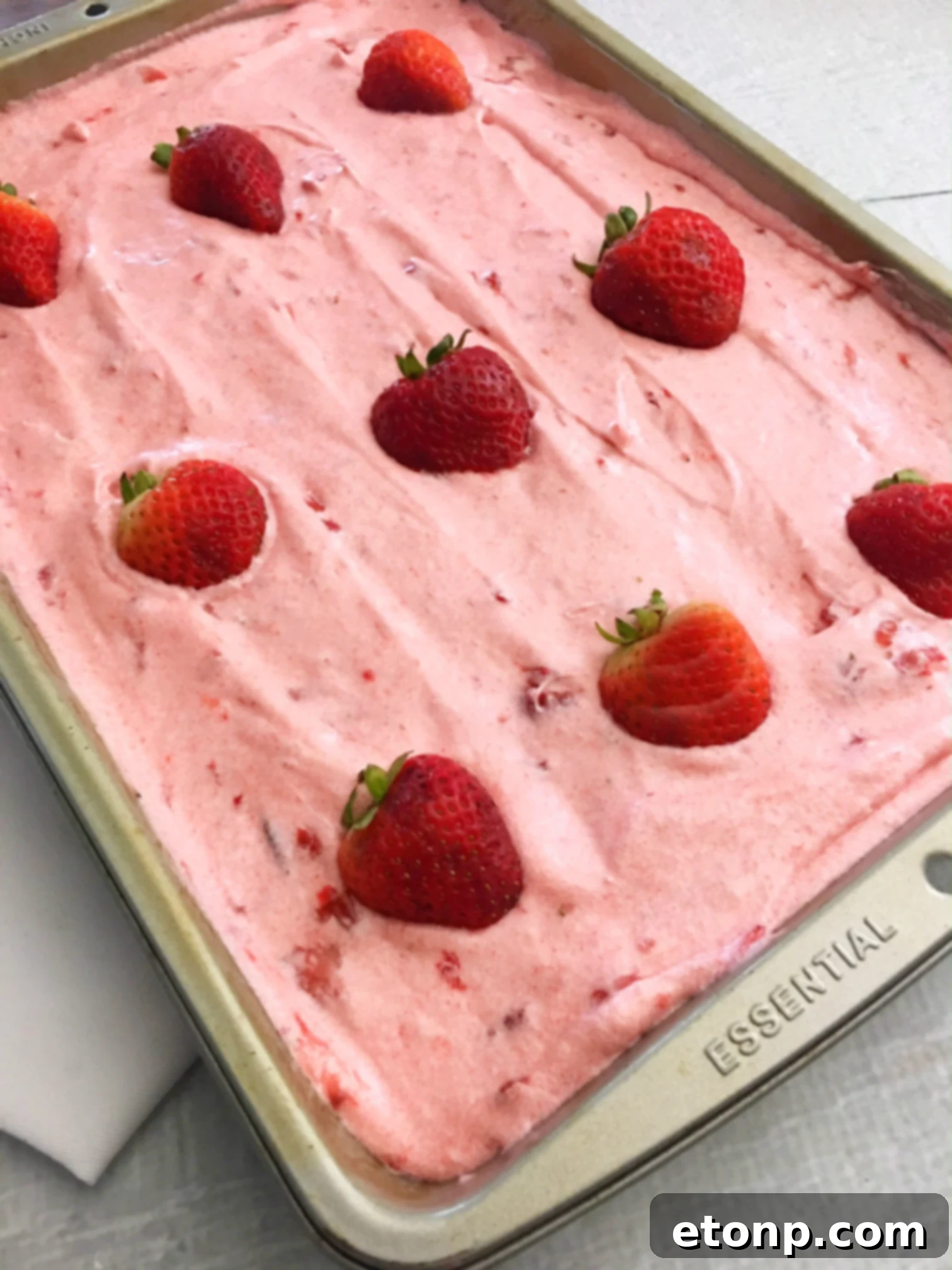Close-up side view of a slice of Strawberry Jello Cake, showcasing the distinct pink layers and thick, creamy frosting.