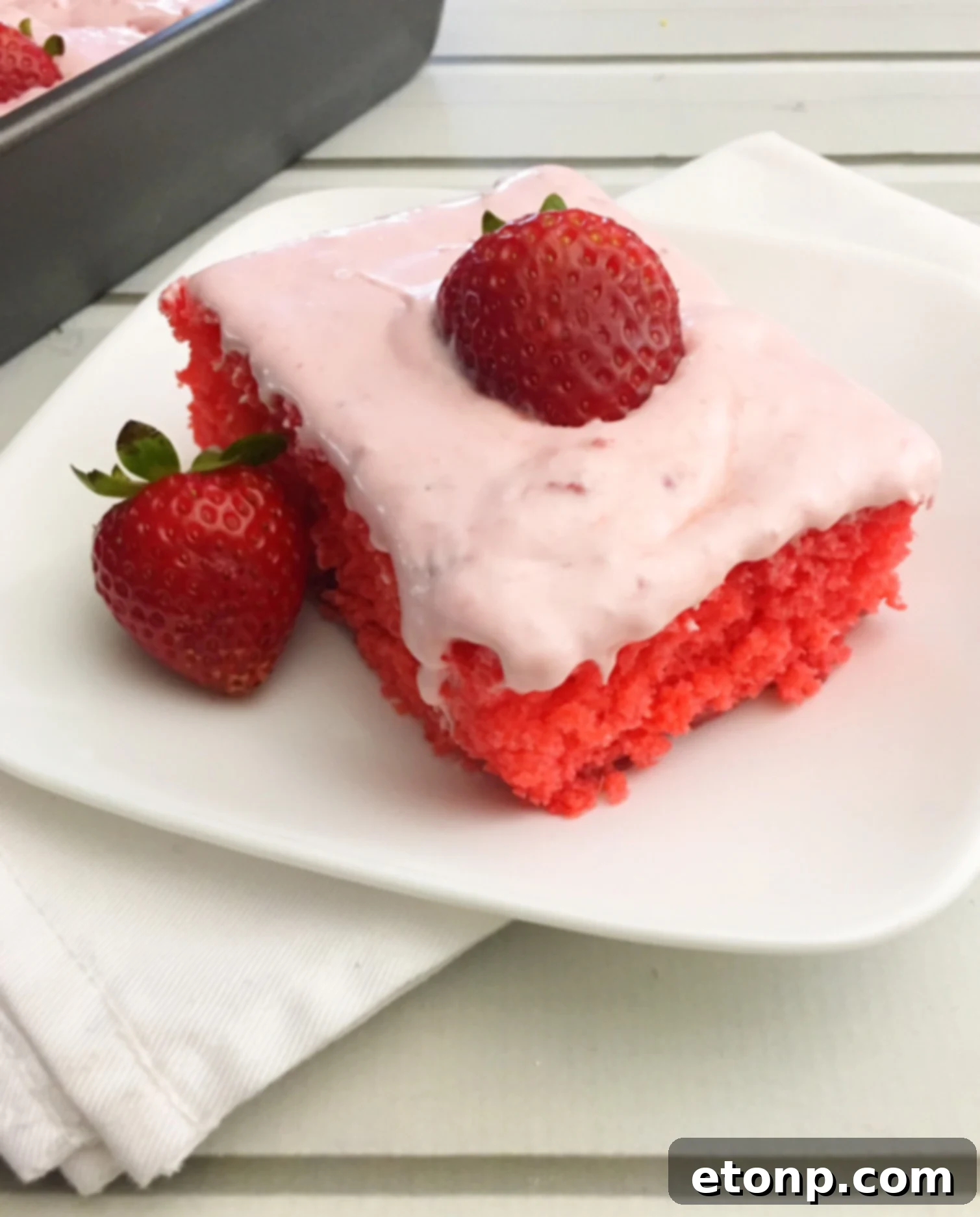 Full Strawberry Jello Cake with a slice removed, revealing the moist pink interior and thick, creamy frosting.