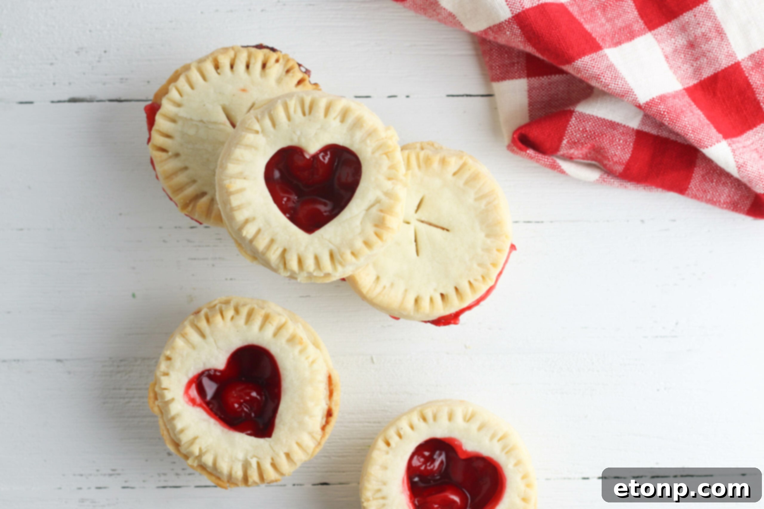 A selection of mini cherry pies, partially removed from a muffin tin and cooling on a wire rack