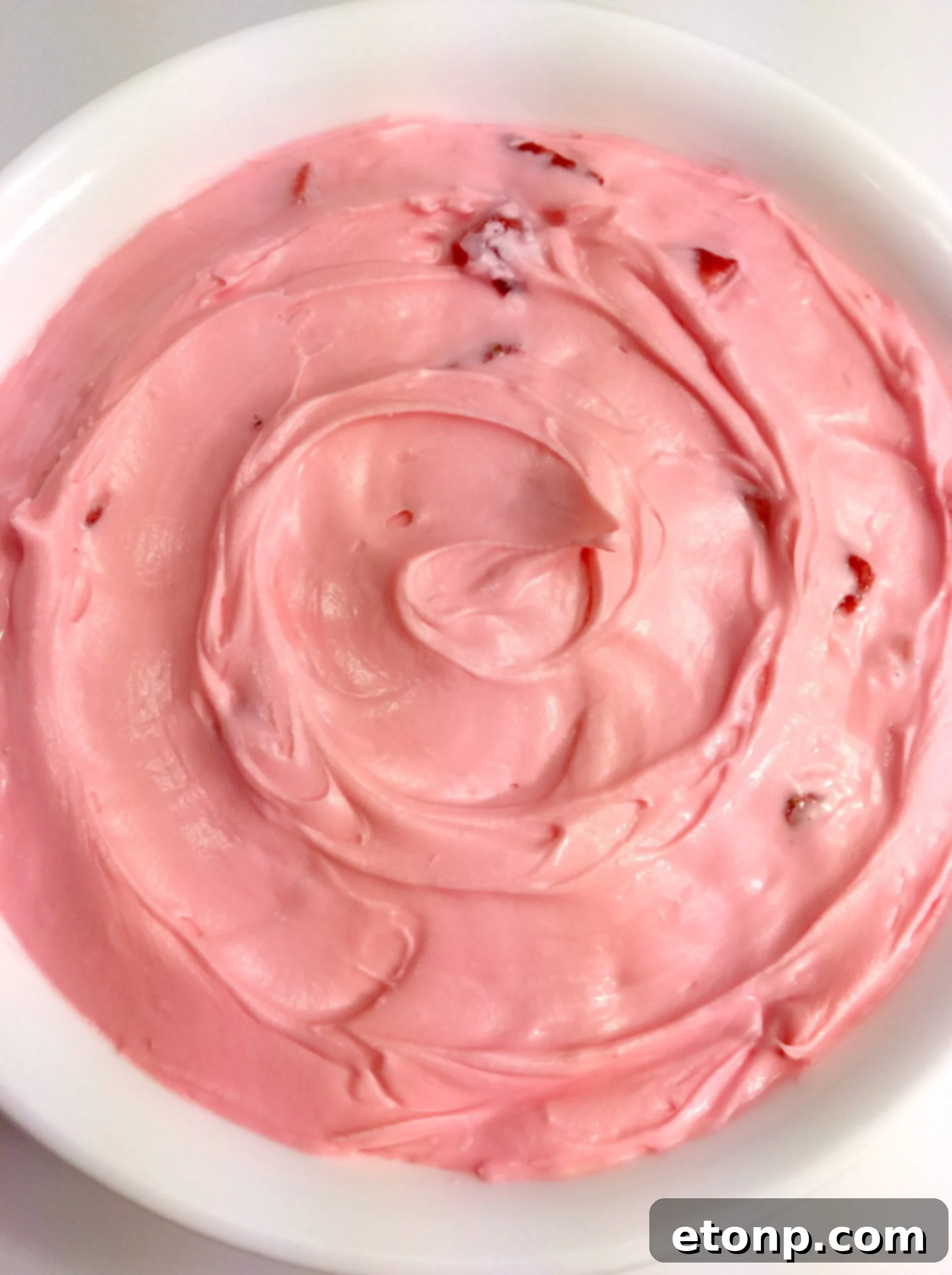 Vibrant pink strawberry buttercream frosting swirled on a cupcake.