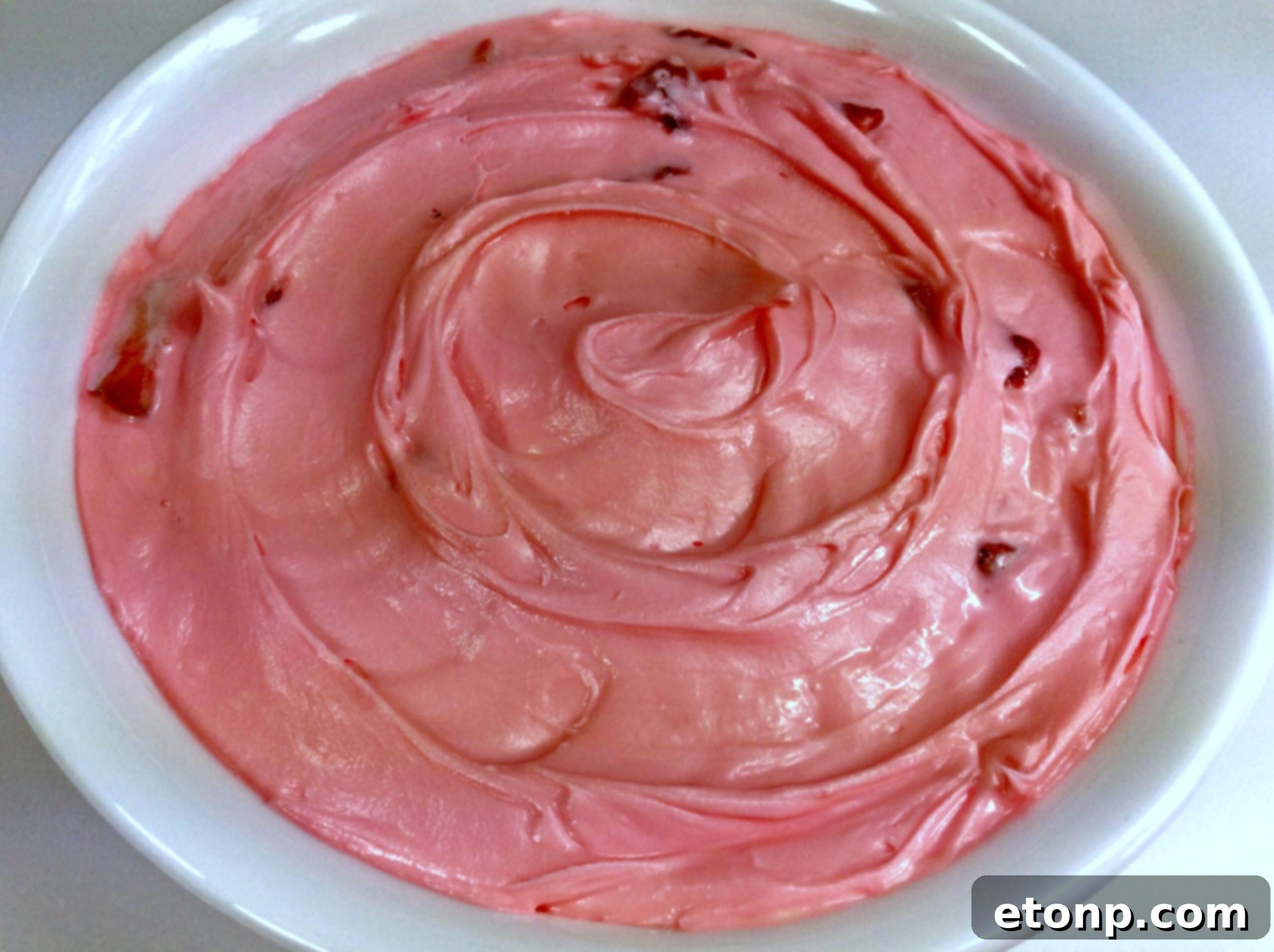 Strawberry buttercream frosting piped generously onto a vanilla cake.