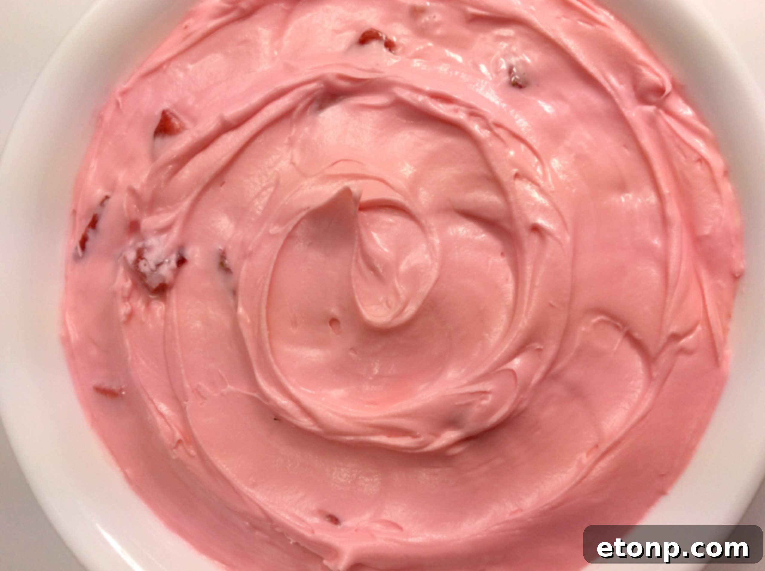 A beautifully frosted strawberry cupcake with real strawberry slices on top.