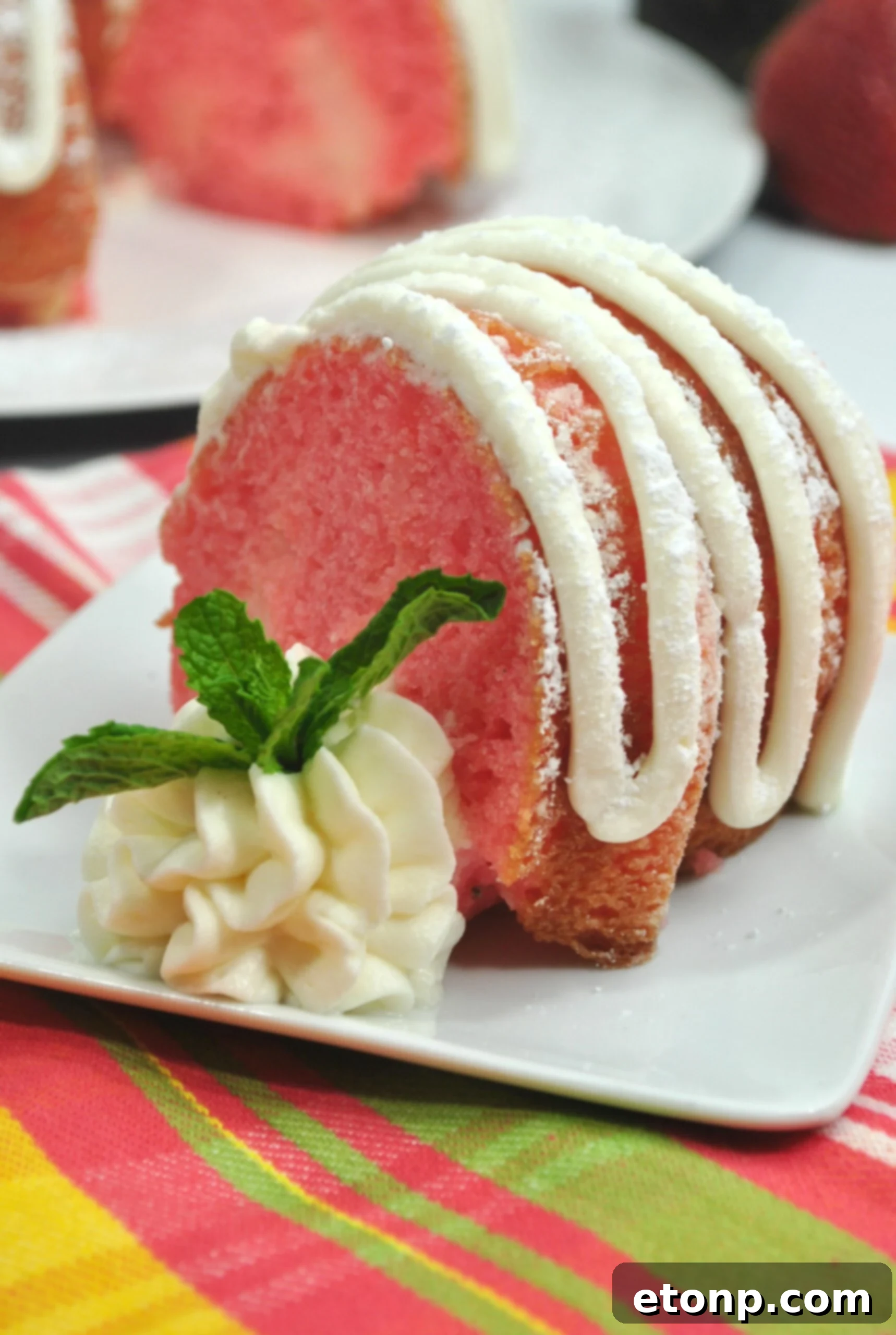 Another enticing angle of the Strawberries & Cream Bundt Cake, showcasing its elegant bundt shape and the artful drizzle of cream cheese frosting, hinting at the deliciousness within.