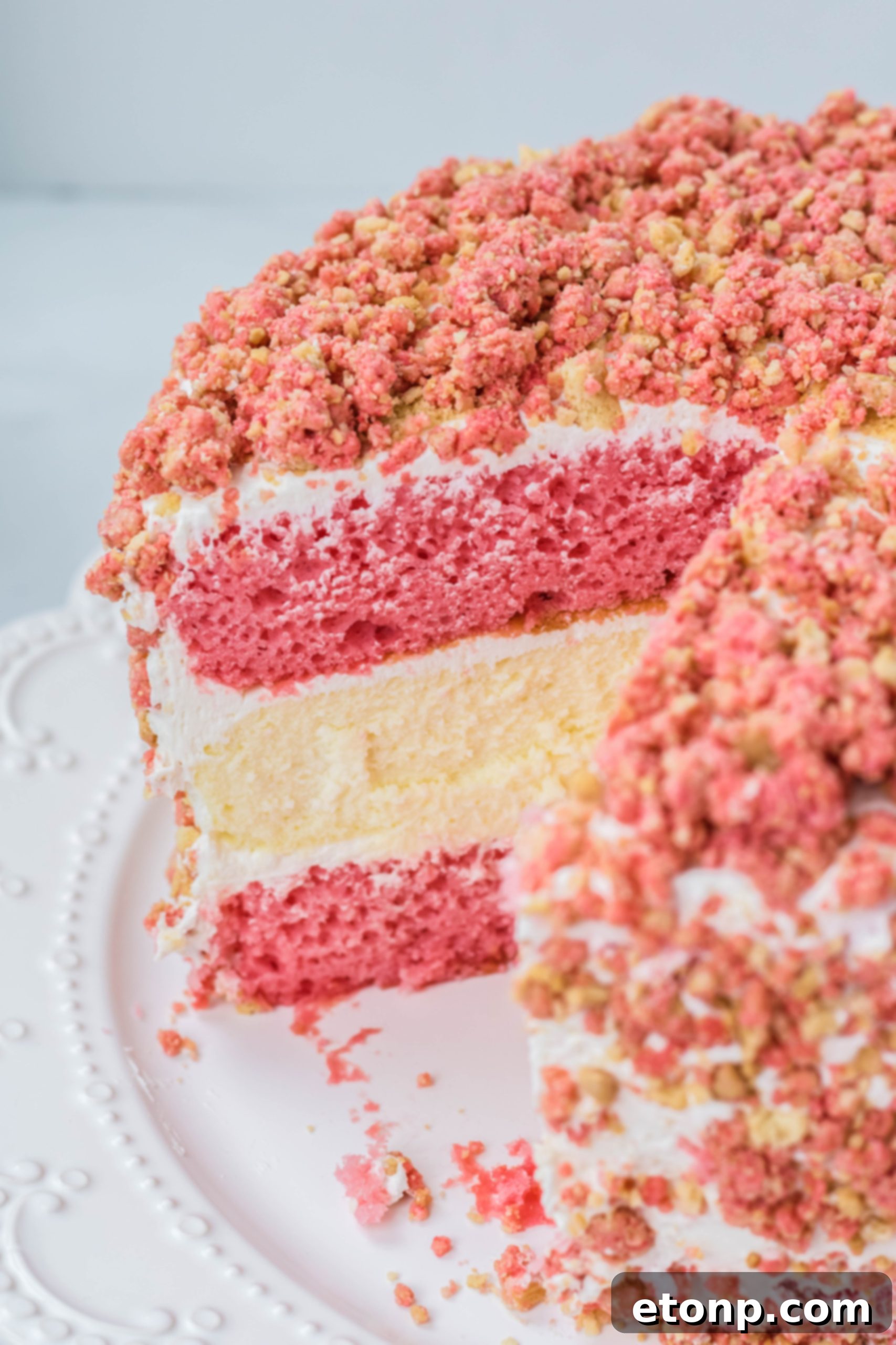 Strawberry Shortcake Cheesecake Cake on a white serving cake dish with a slice missing 