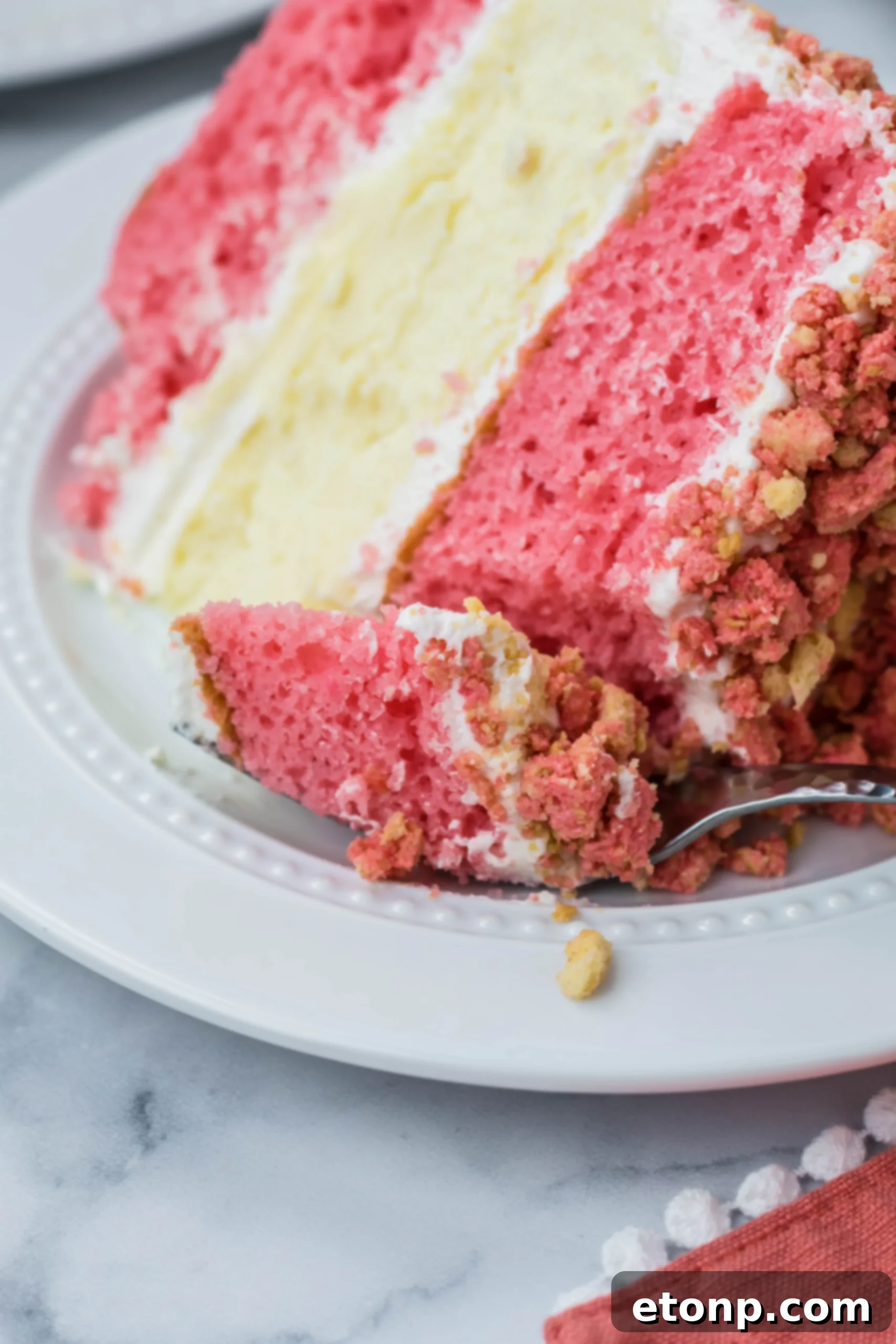 Up close shot of the Strawberry Shortcake Cheesecake Cake slice on a white plate with a fork taking a bite out 