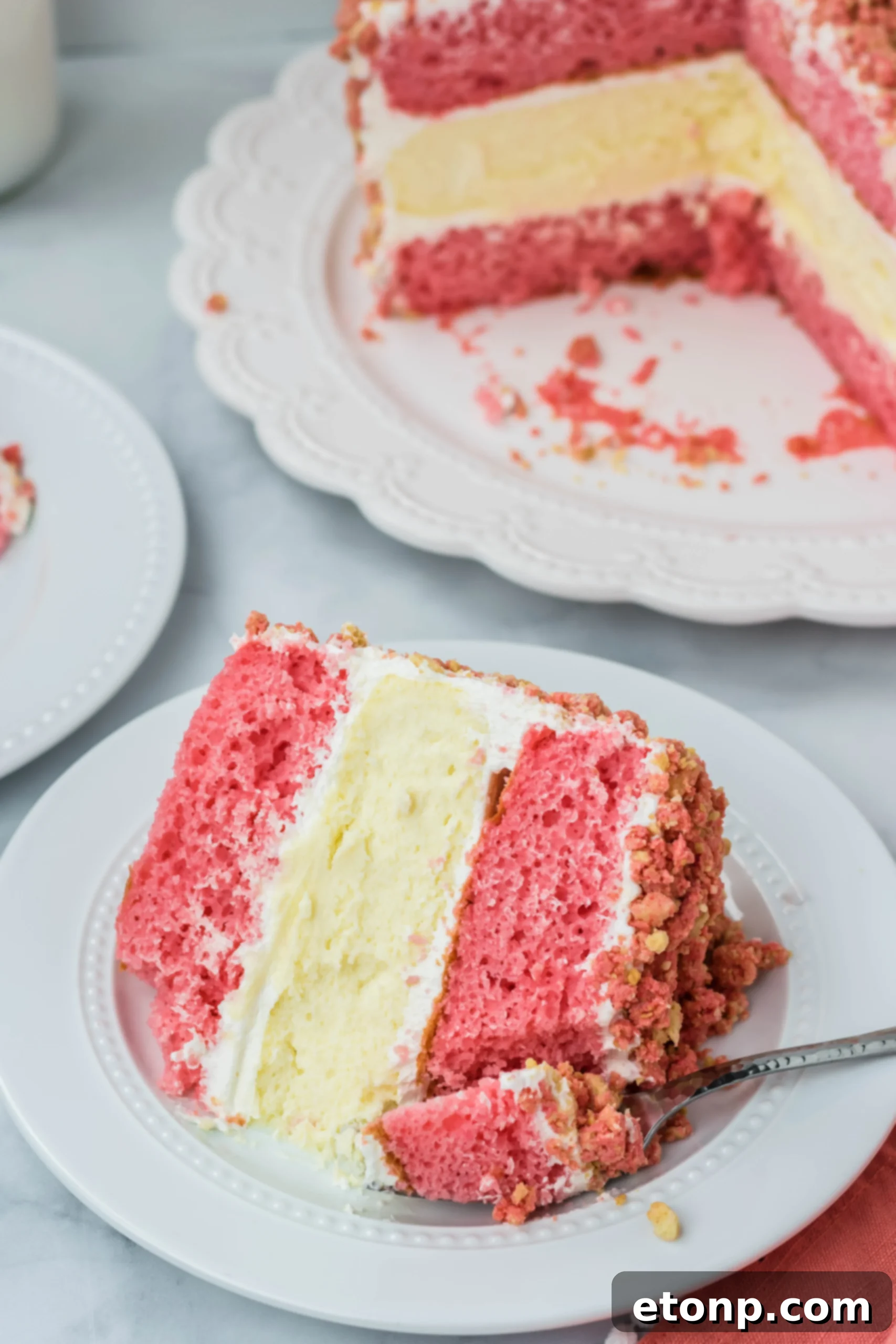 overhead shot of the Strawberry Shortcake Cheesecake Cake on a white plate with a fork taking a bite out 