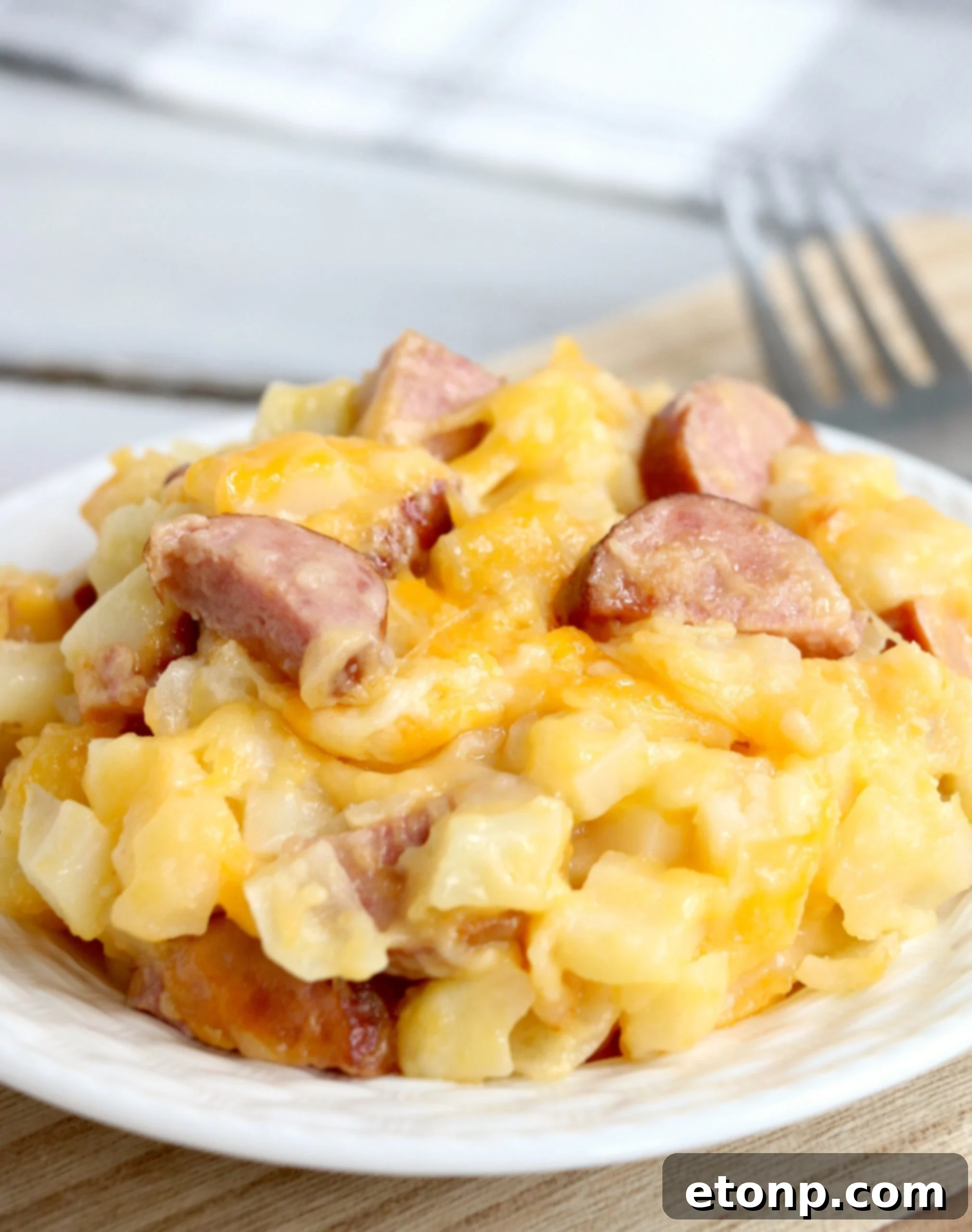 A close-up of the Slow Cooker Cheesy Kielbasa Hashbrown Casserole, showing golden brown hashbrowns, slices of kielbasa, and melted, bubbly cheese in a slow cooker, ready to be served.