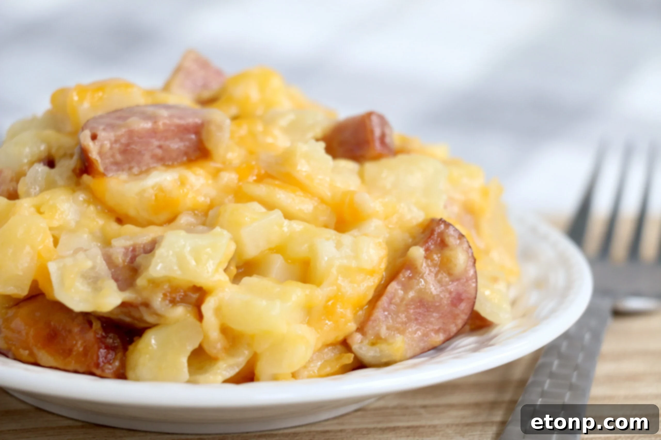 A serving spoon lifting a generous portion of the Cheesy Kielbasa Hashbrown Casserole from the slow cooker, clearly showing the gooey melted cheese and chunky pieces of kielbasa and hashbrowns.