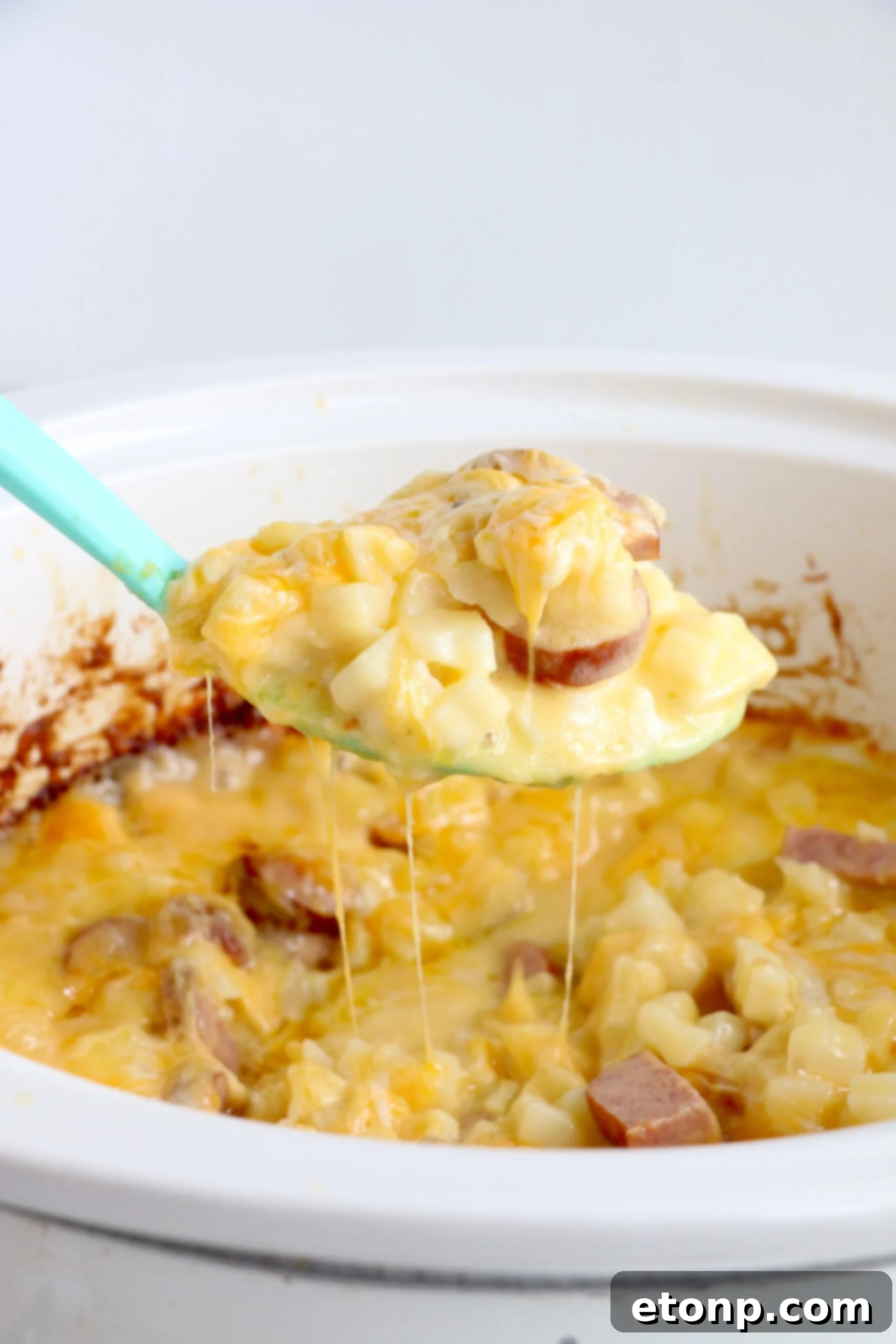 A closer view of the Cheesy Kielbasa Hashbrown Casserole still in the slow cooker, highlighting the texture of the tender hashbrowns and the golden-brown, bubbling crust of the melted cheese on top.