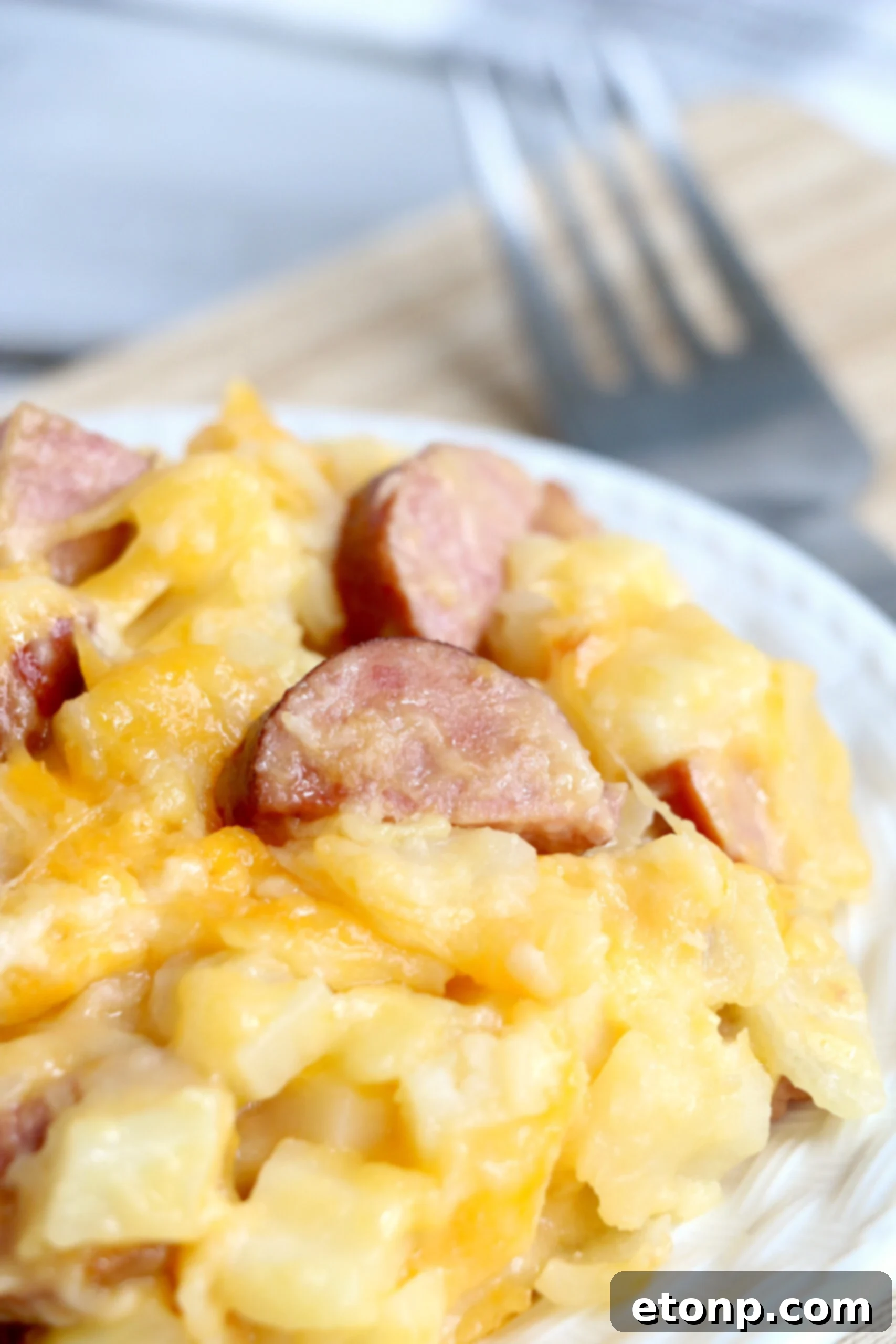 A close-up of a single portion of the Slow Cooker Cheesy Kielbasa Hashbrown Casserole served on a crisp white plate, elegantly garnished with fresh chopped parsley.