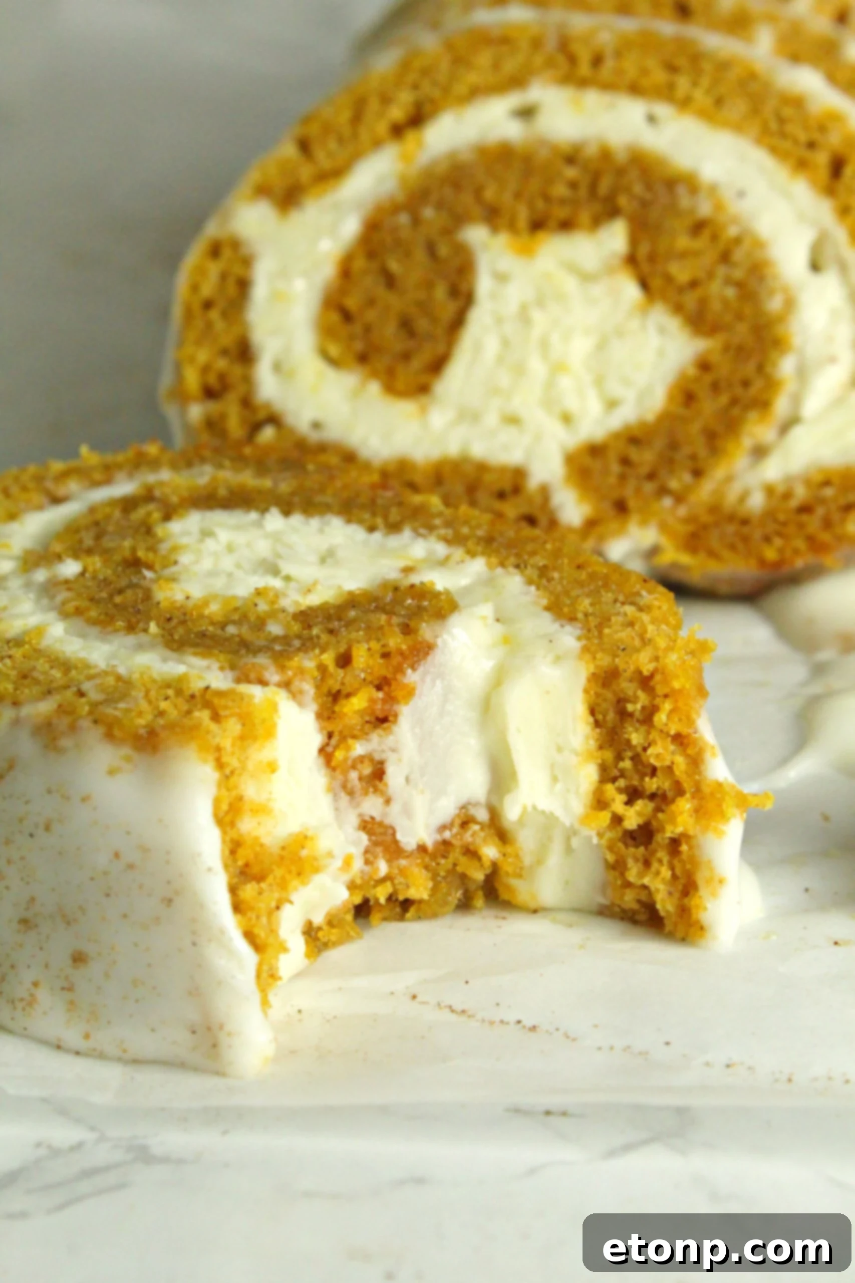 Close-up of a beautifully sliced pumpkin cake roll with cream cheese frosting swirls, showcasing its moist texture and rich orange color.