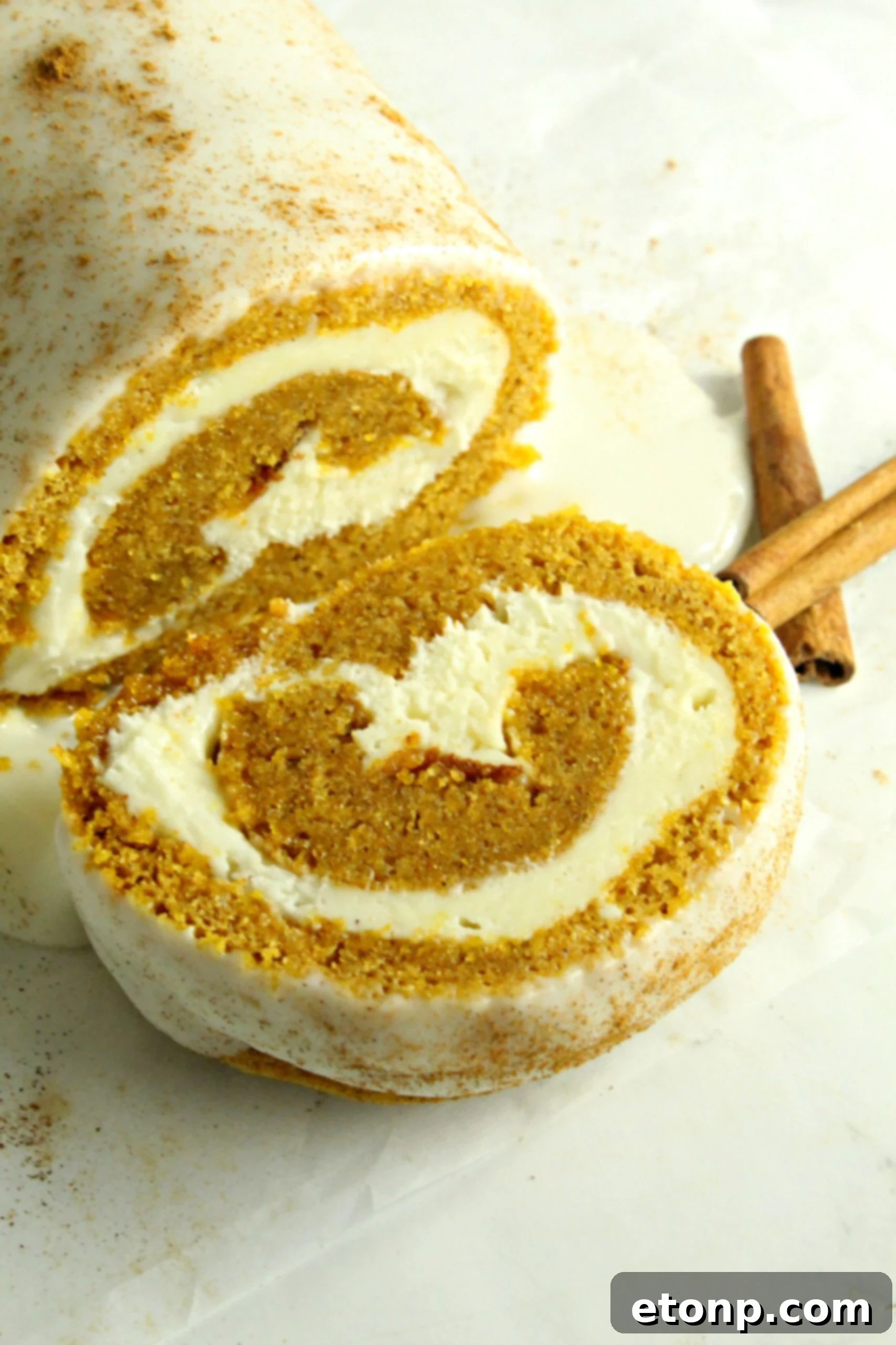 A close-up of a pumpkin roll slice, highlighting the beautiful spiral and the generous layer of cream cheese frosting.