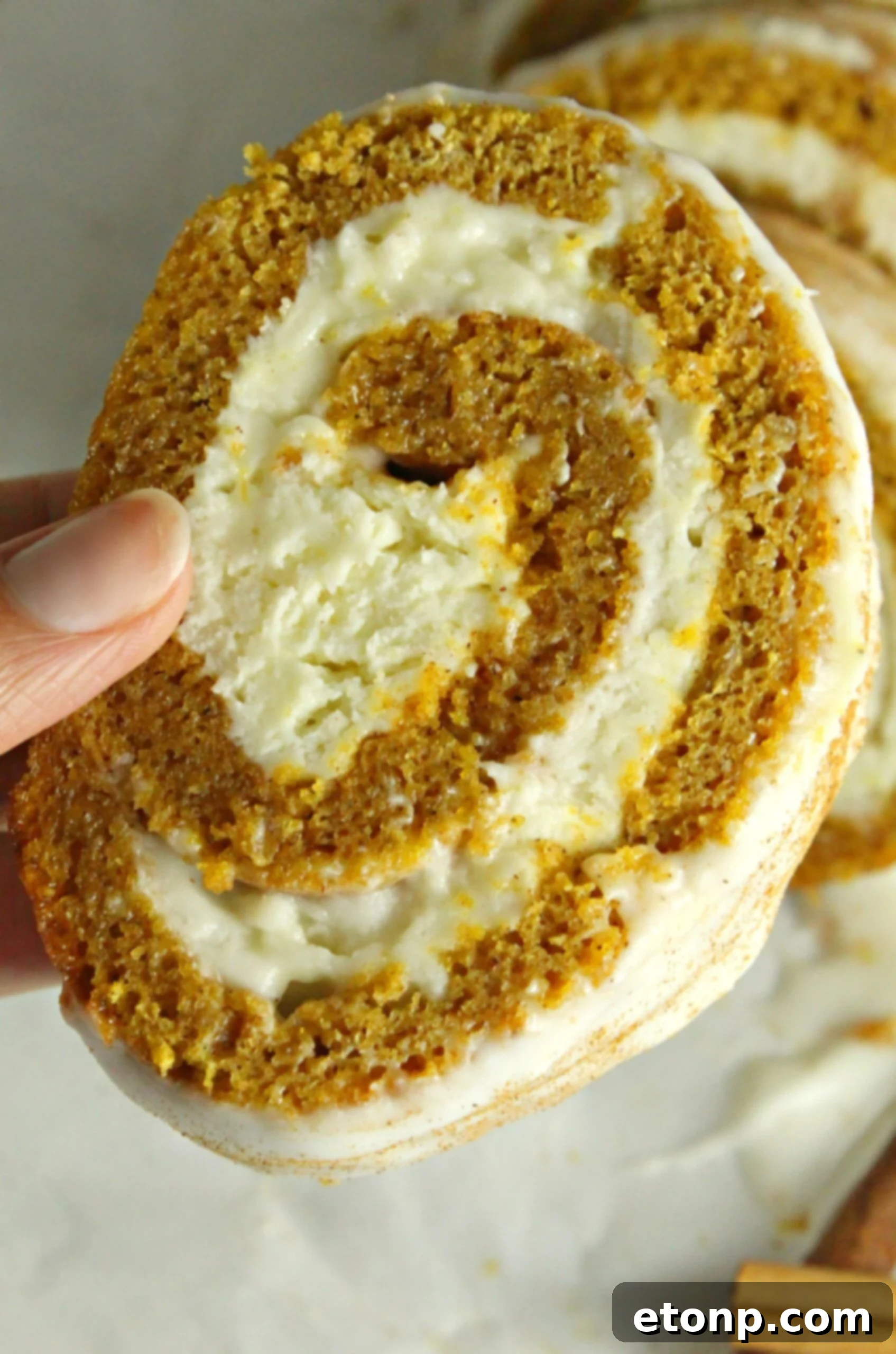 A hand gently unrolling a pumpkin cake, covered in powdered sugar on a kitchen towel.