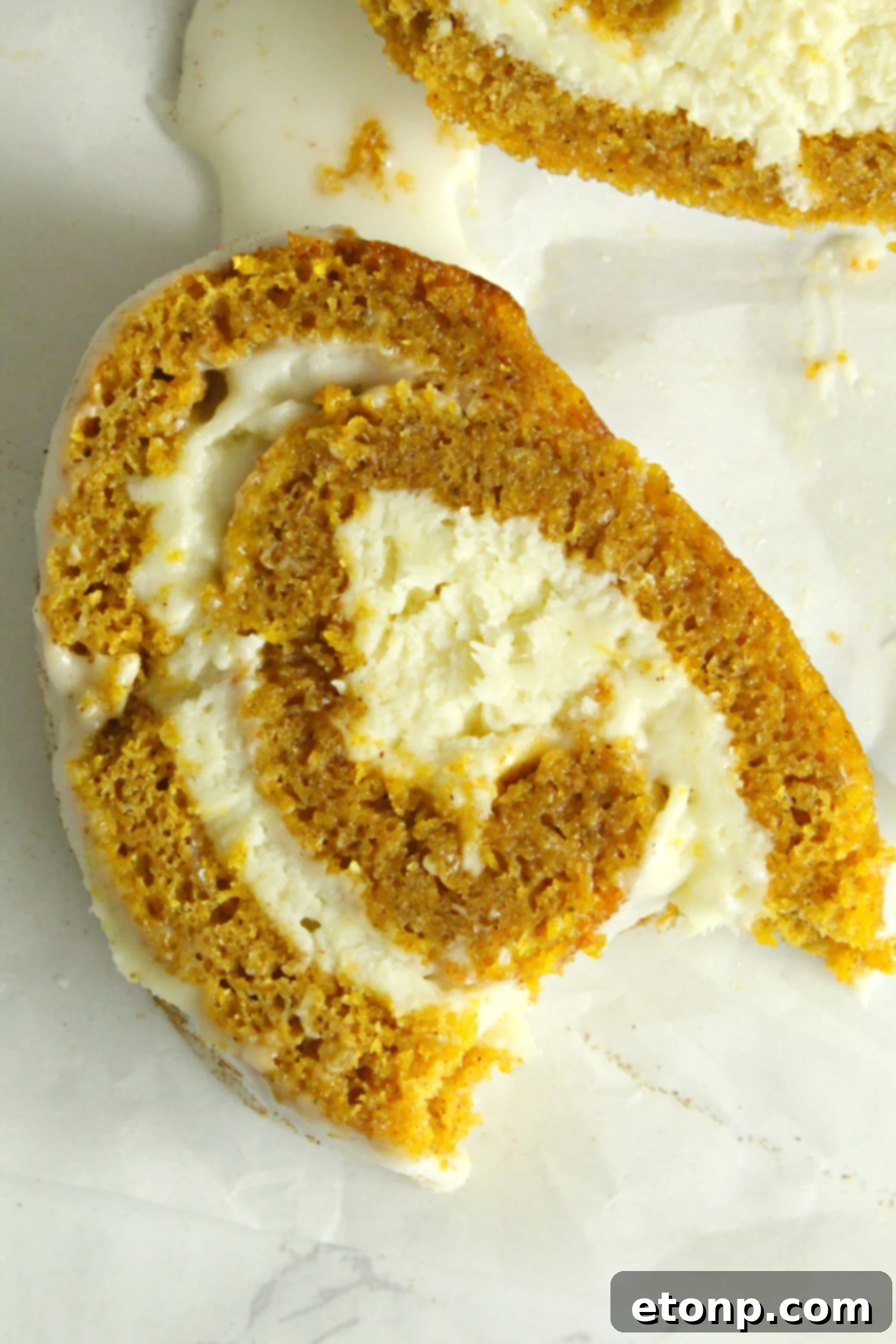 Close-up of the smooth, rich cream cheese frosting being spread evenly onto the unrolled pumpkin cake.