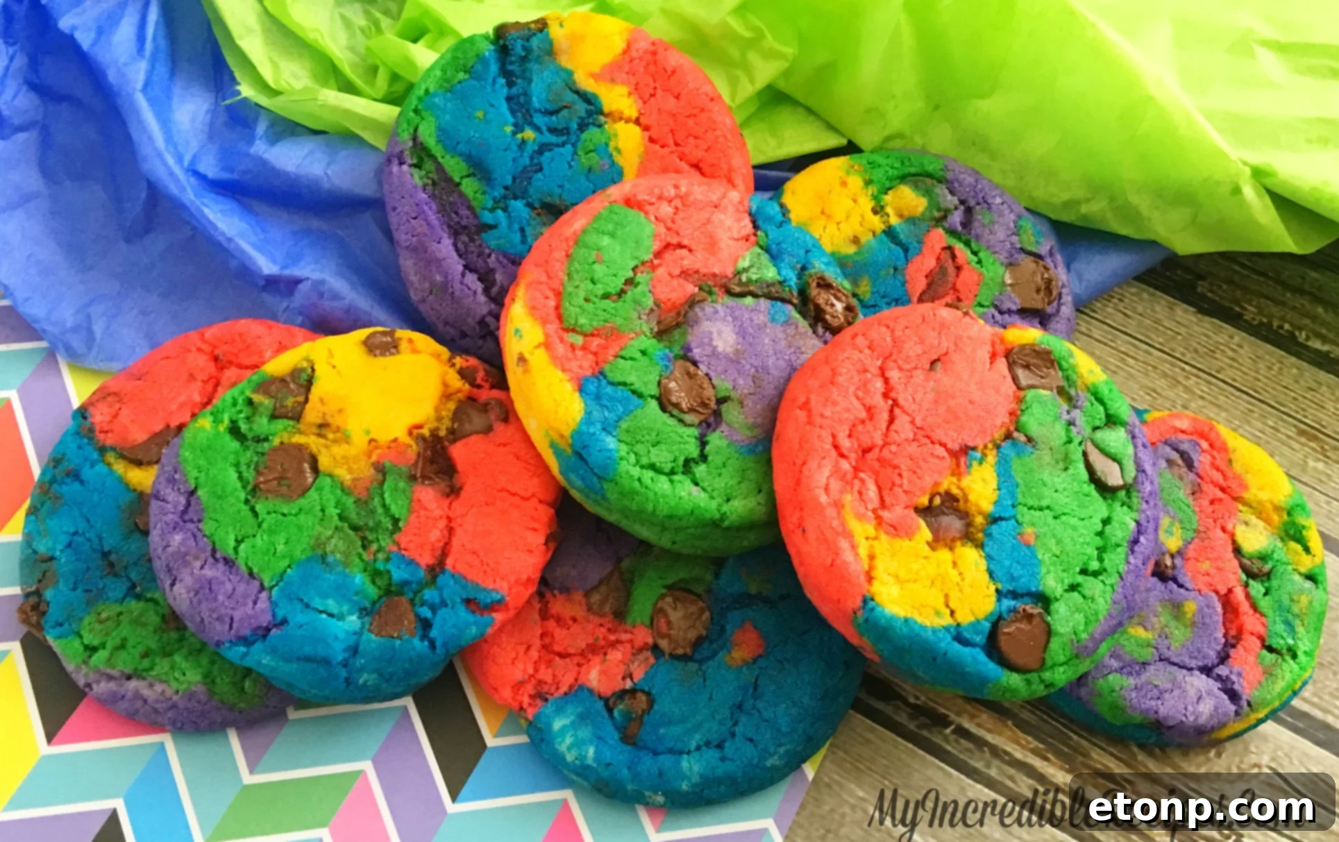 A plate piled high with various homemade rainbow chocolate chip cookies, ready to be enjoyed