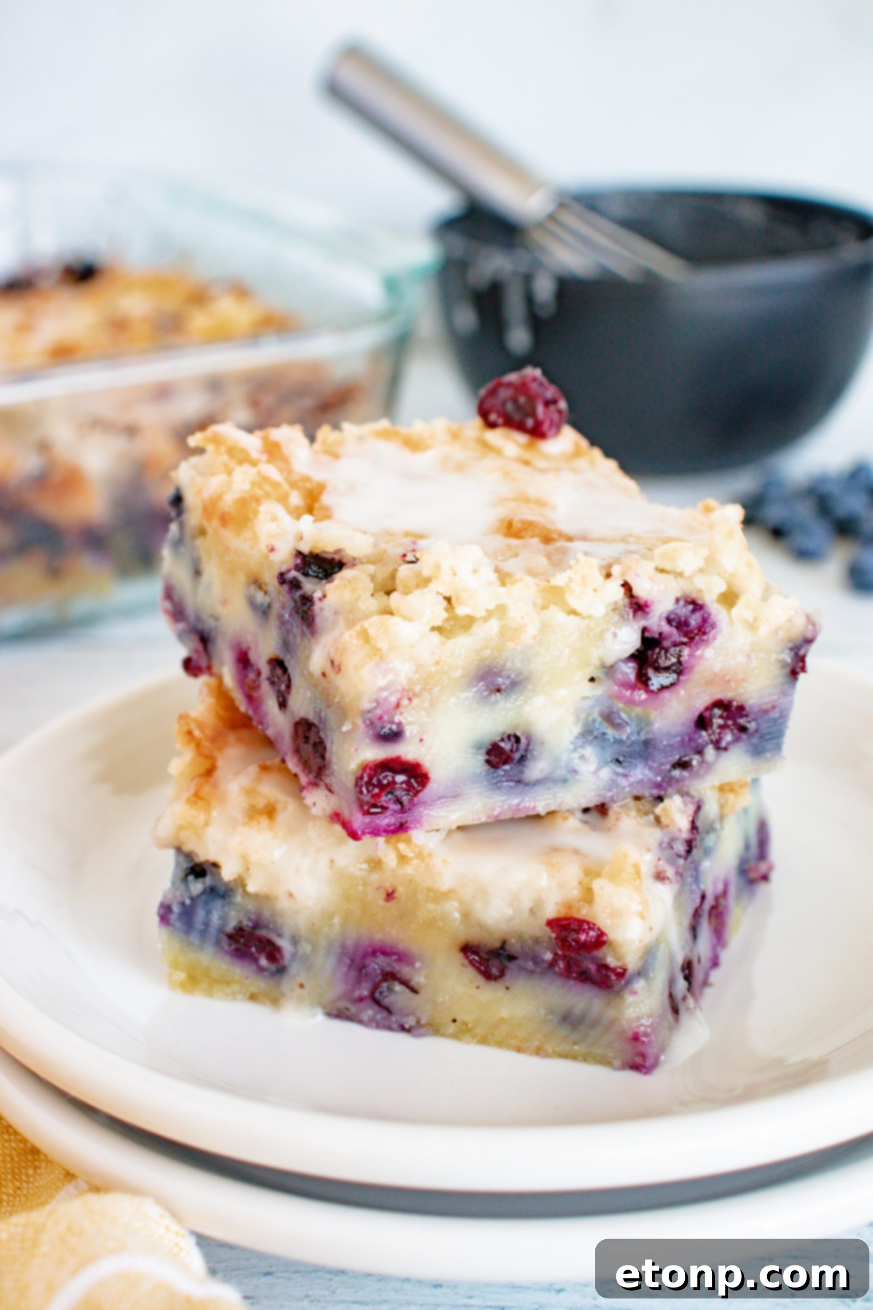 Close-up of a slice of moist blueberry muffin cake with streusel topping and vanilla glaze on a white plate