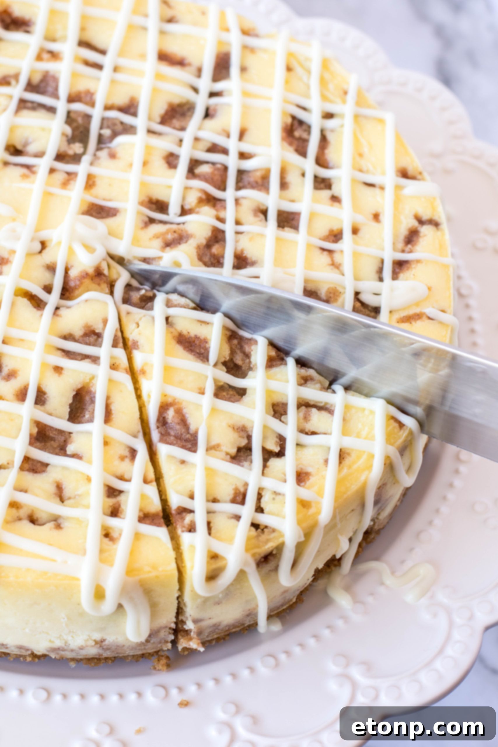 Close-up of a whole Cinnamon Roll Cheesecake, showcasing its thick, creamy texture and generous cream cheese drizzle.