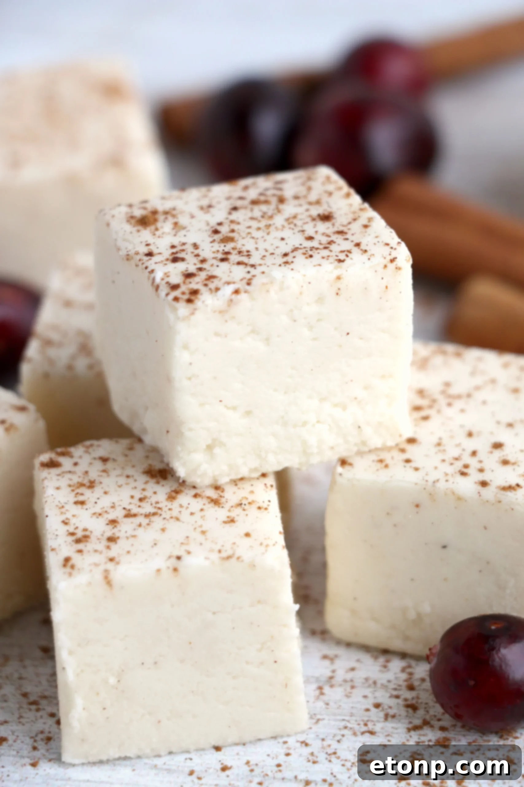 Multiple pieces of eggnog fudge stacked on a festive plate, dusted with cinnamon.