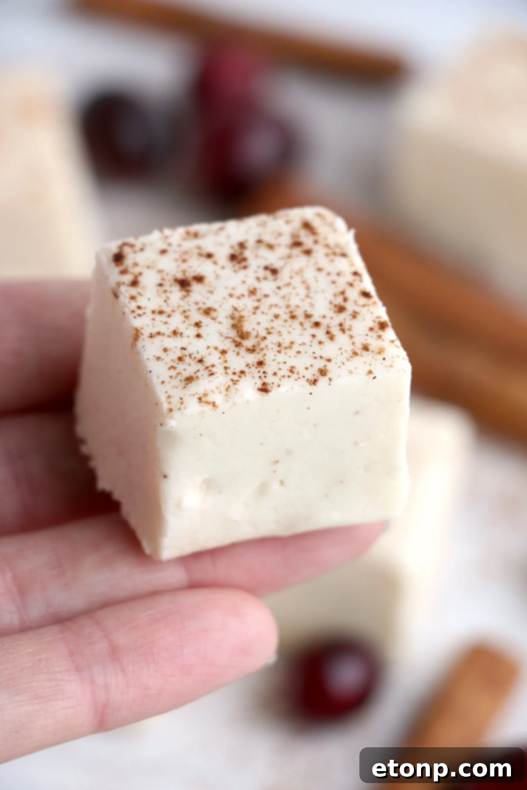 Eggnog fudge on a cutting board, ready to be sliced, garnished with a light dusting of cinnamon.