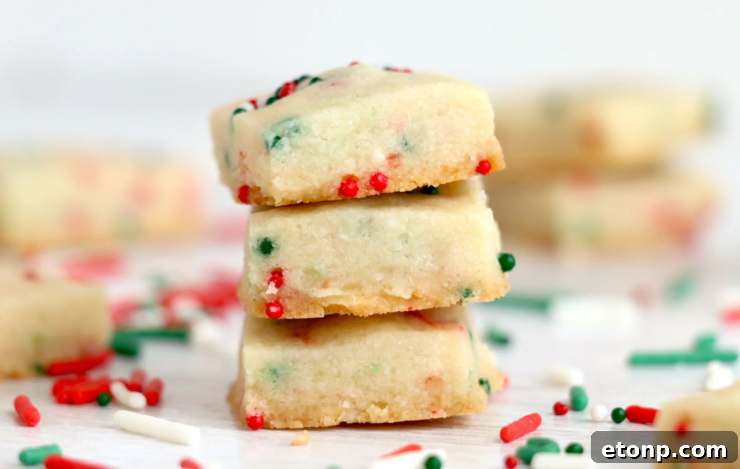 A hand reaching for a Christmas Shortbread Cookie Bite from a festive plate.