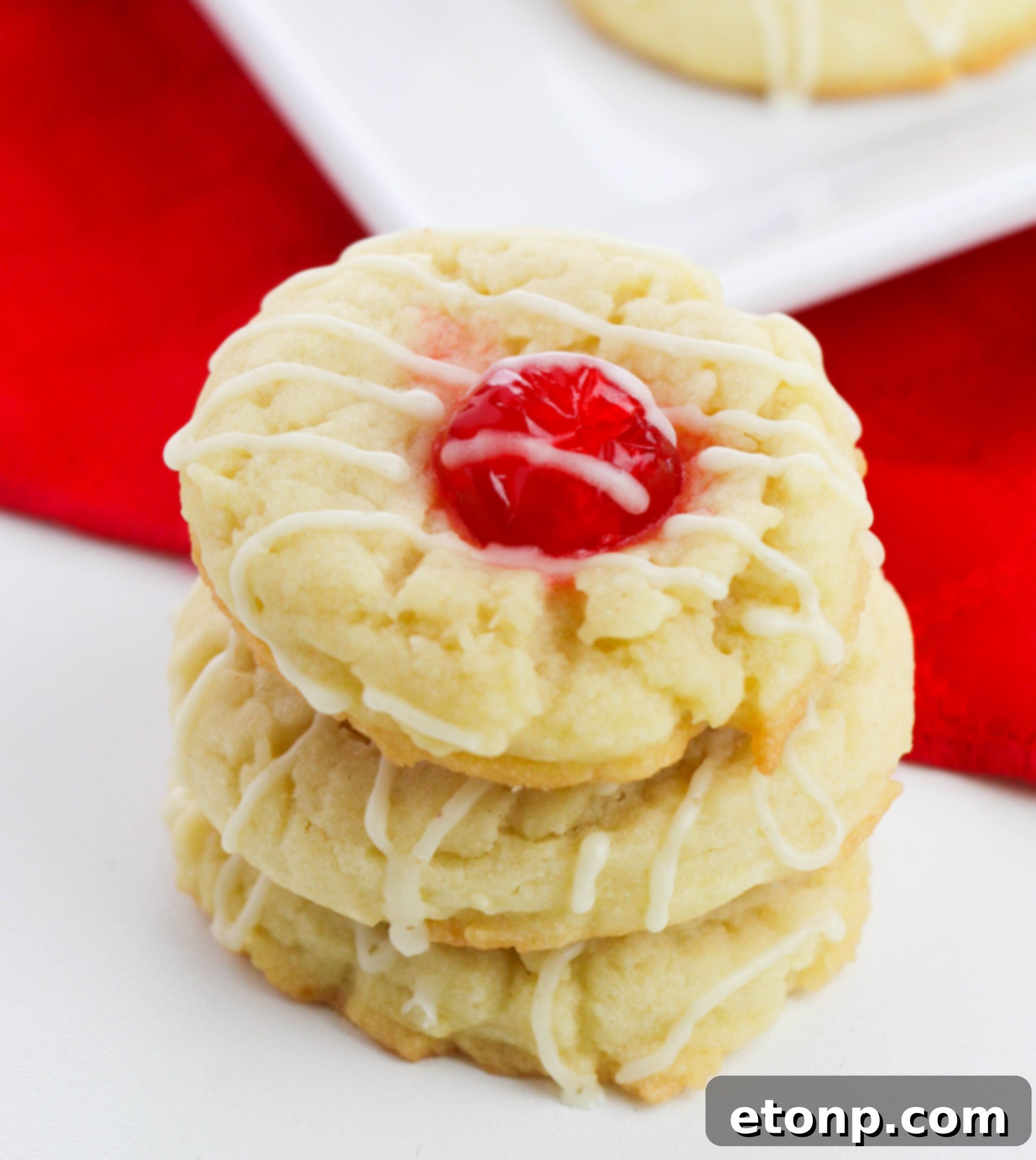Close-up of freshly baked Eggnog Thumbprint Cookies with bright red maraschino cherry centers and a sweet icing drizzle.