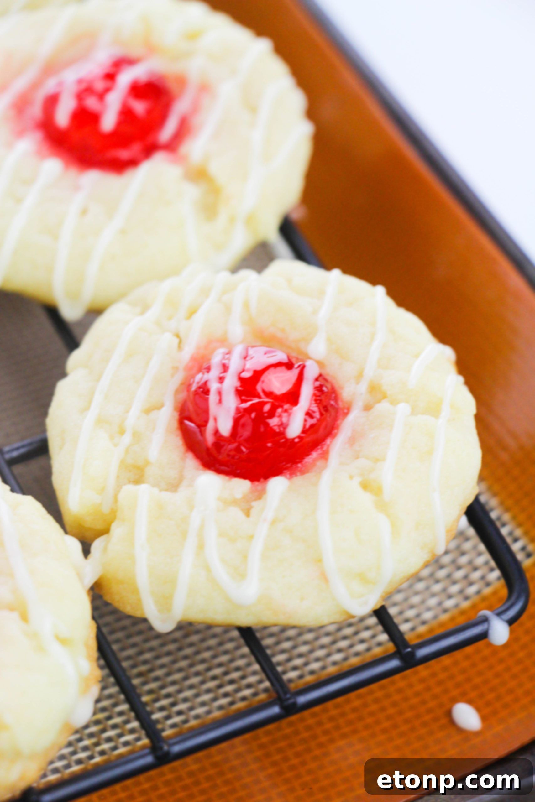 Eggnog Thumbprint Cookies cooling on a wire rack, highlighting the golden edges and cherry filling before icing.