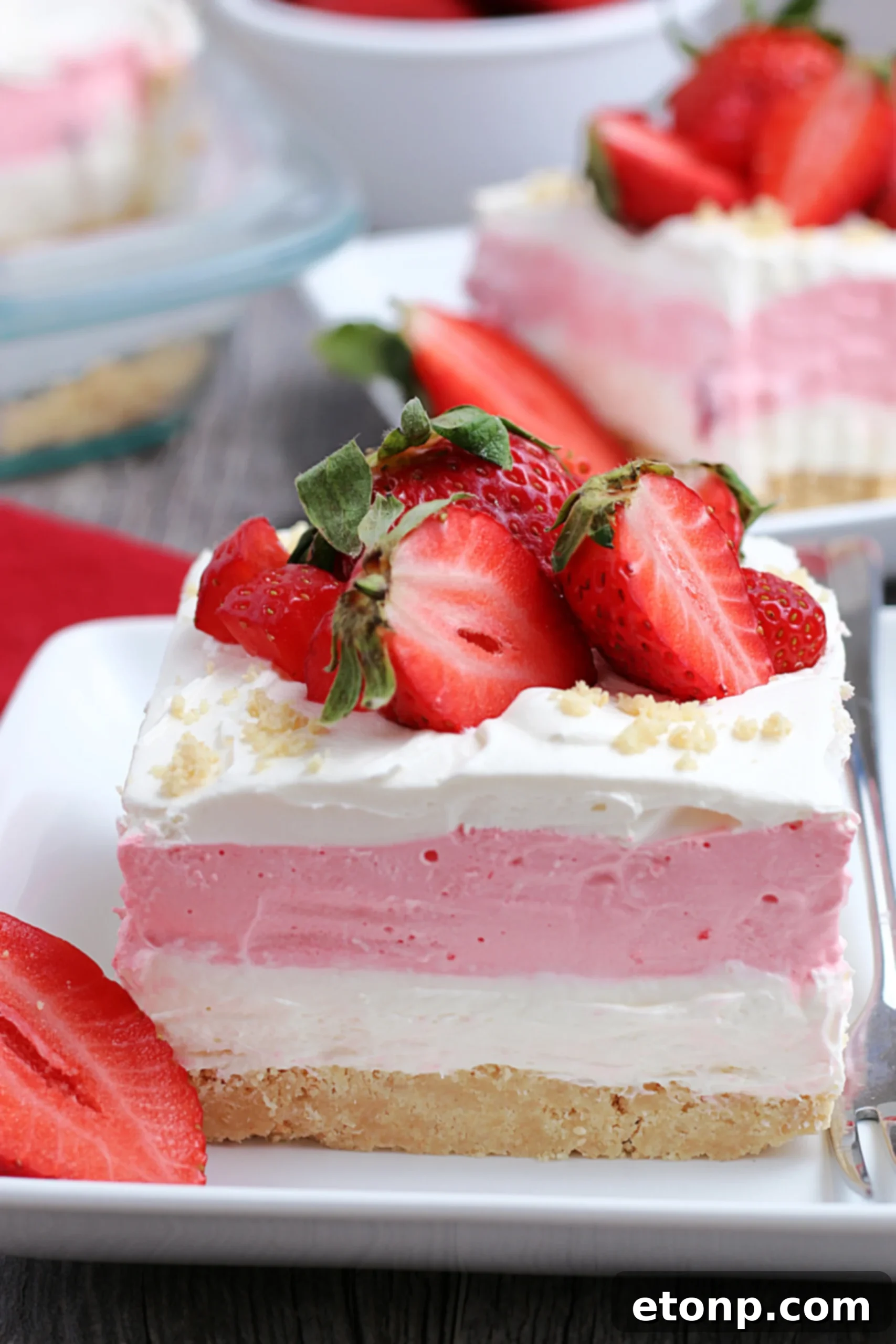 A close-up of the multi-layered Strawberry Cheesecake Lasagna, showing the distinct pink and white layers with fresh strawberry pieces embedded.