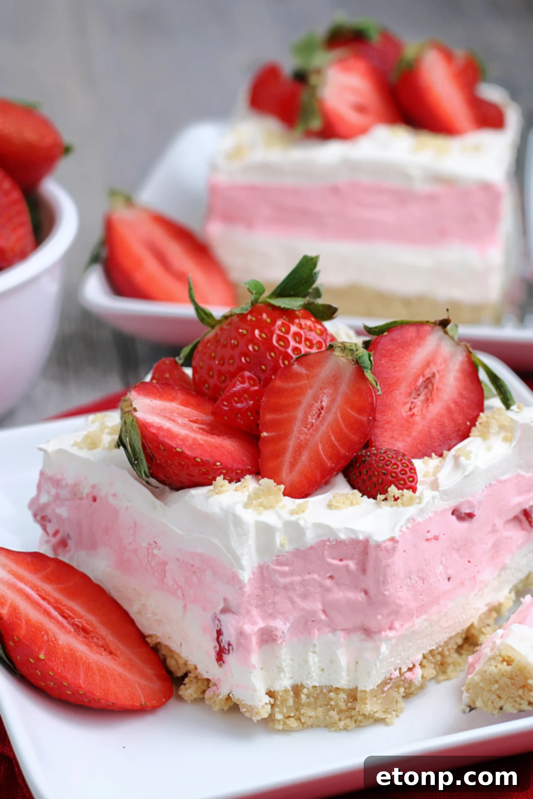 A beautifully presented slice of Strawberry Cheesecake Lasagna on a white plate, garnished with a whole fresh strawberry and mint.