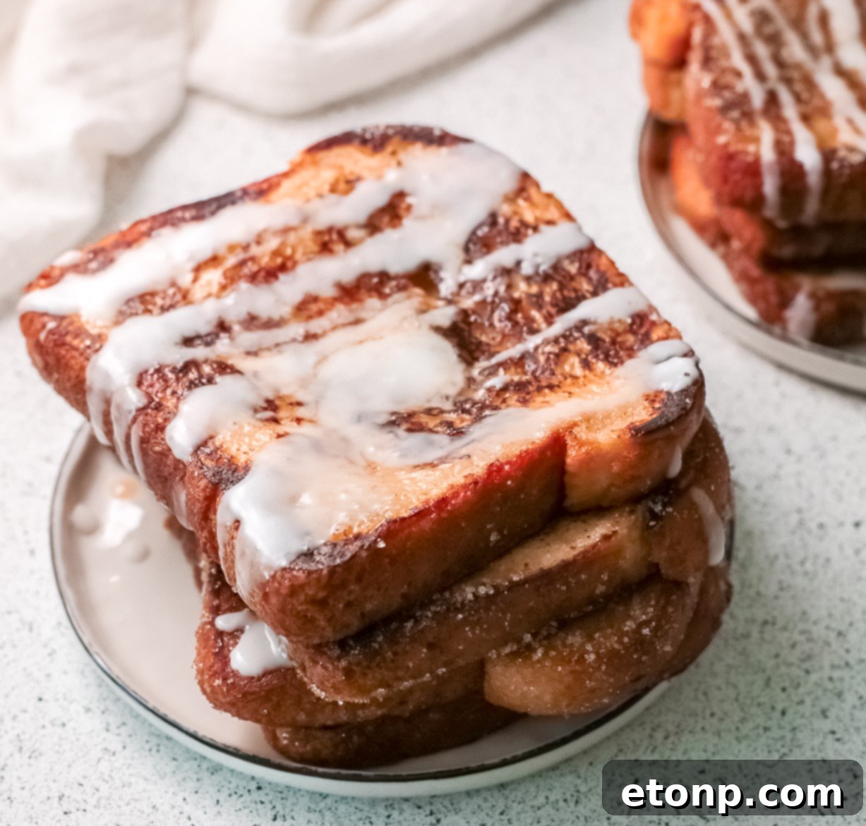 A stack of freshly made Churro French Toast, glistening with cinnamon sugar and icing, ready to be served.