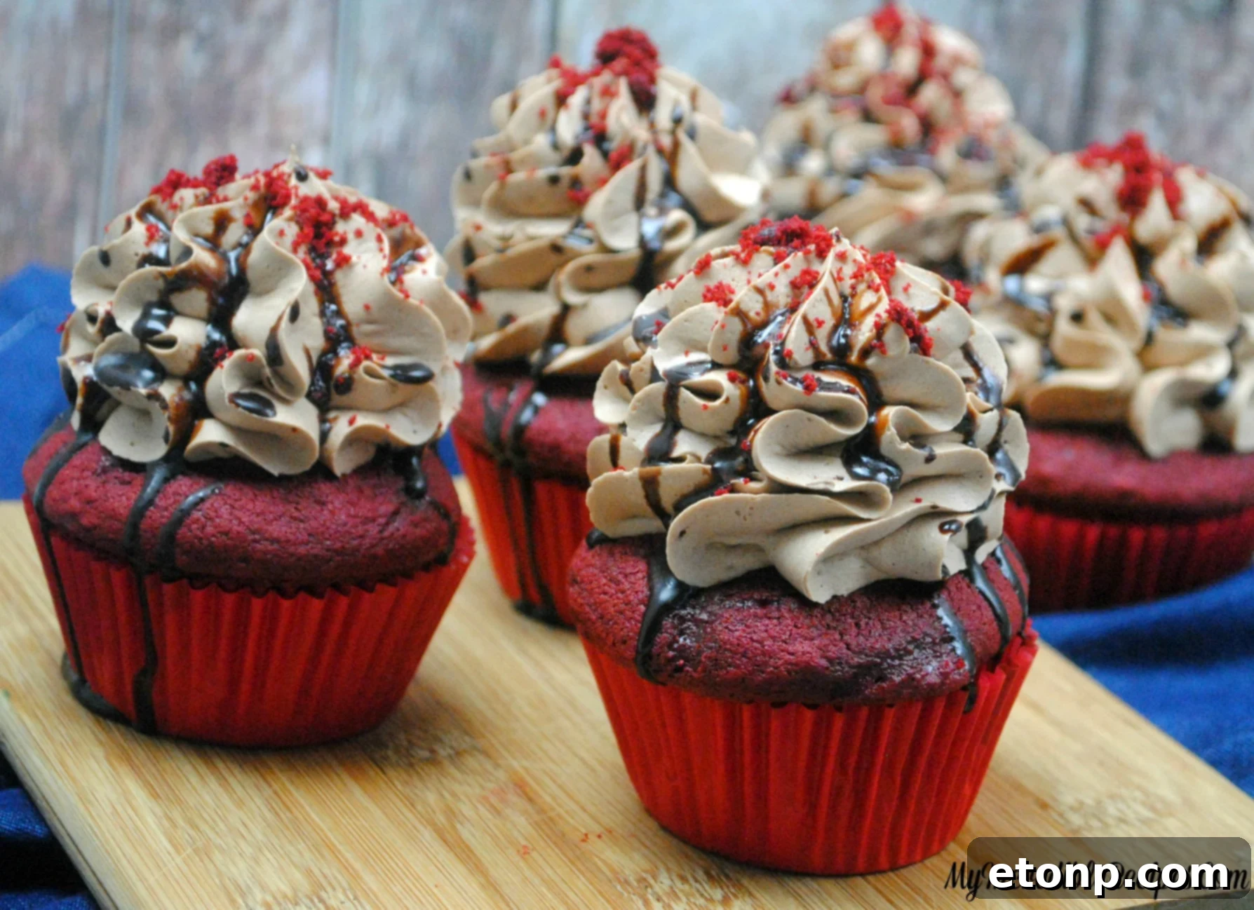 Hot fudge being drizzled artistically over a chocolate cream cheese frosted red velvet cupcake