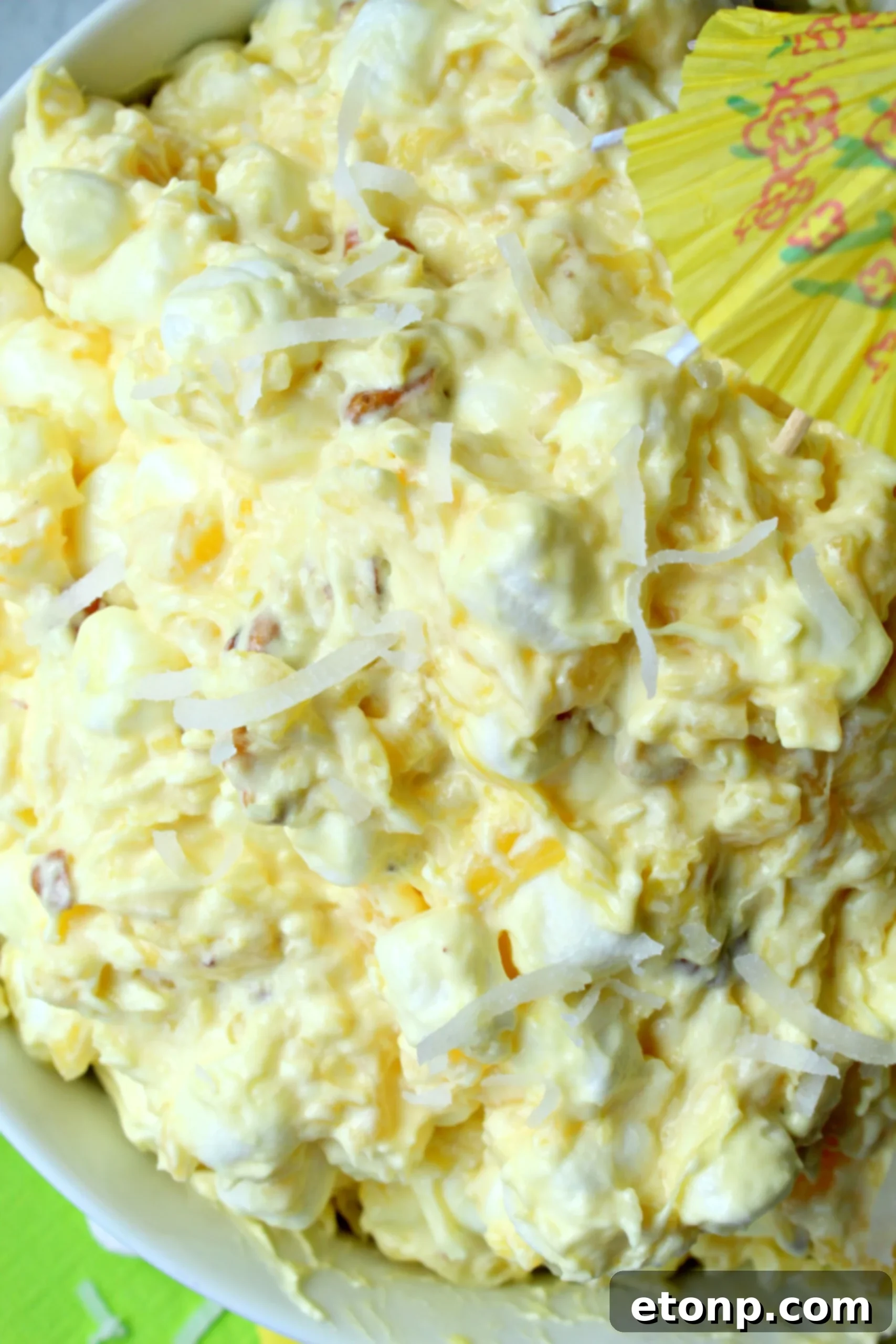 A vibrant bowl of Pina Colada Fluff dessert, garnished with pineapple chunks and coconut flakes, set against a bright, inviting background.