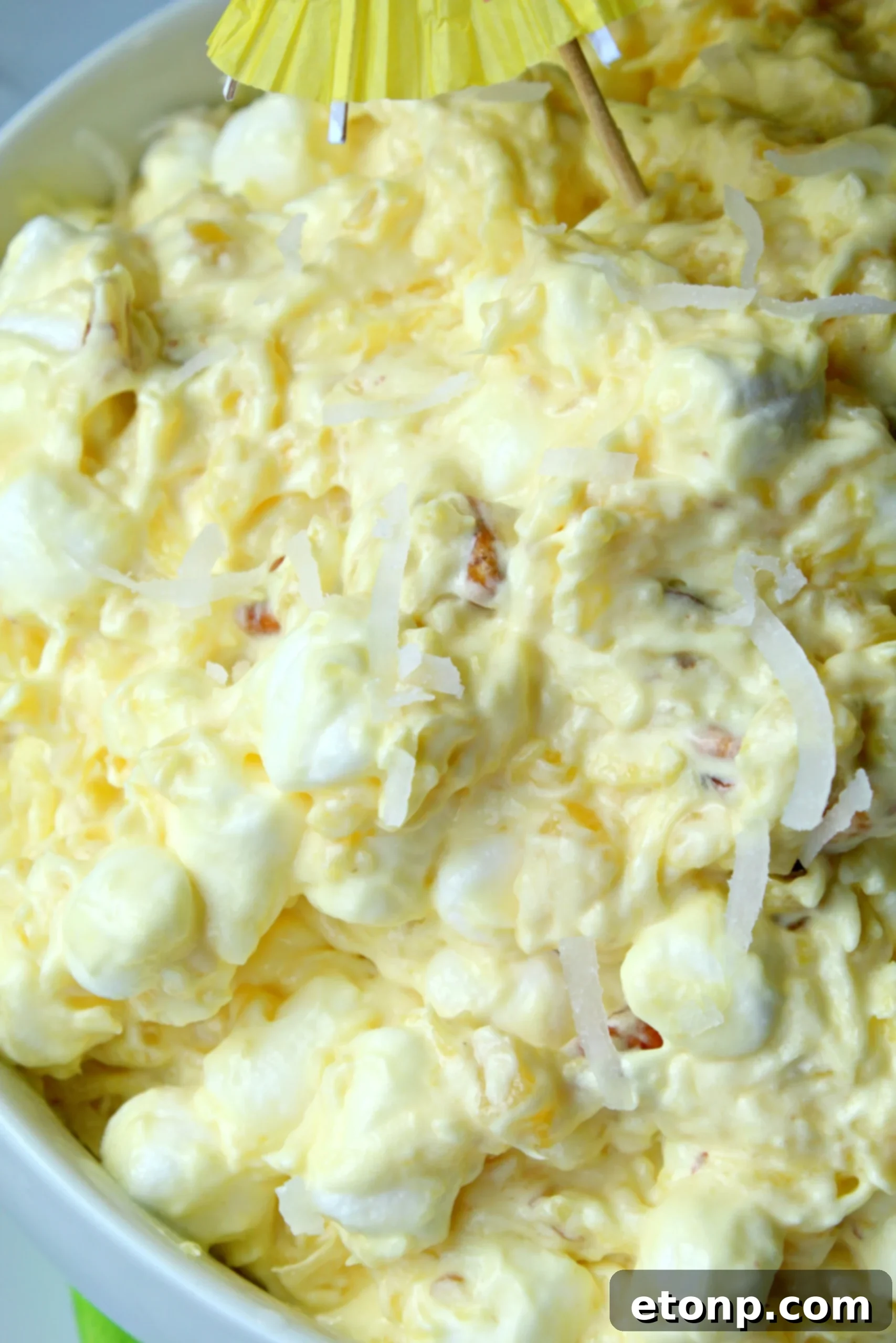 Pina Colada Fluff being scooped from a large bowl, emphasizing its light and airy consistency.
