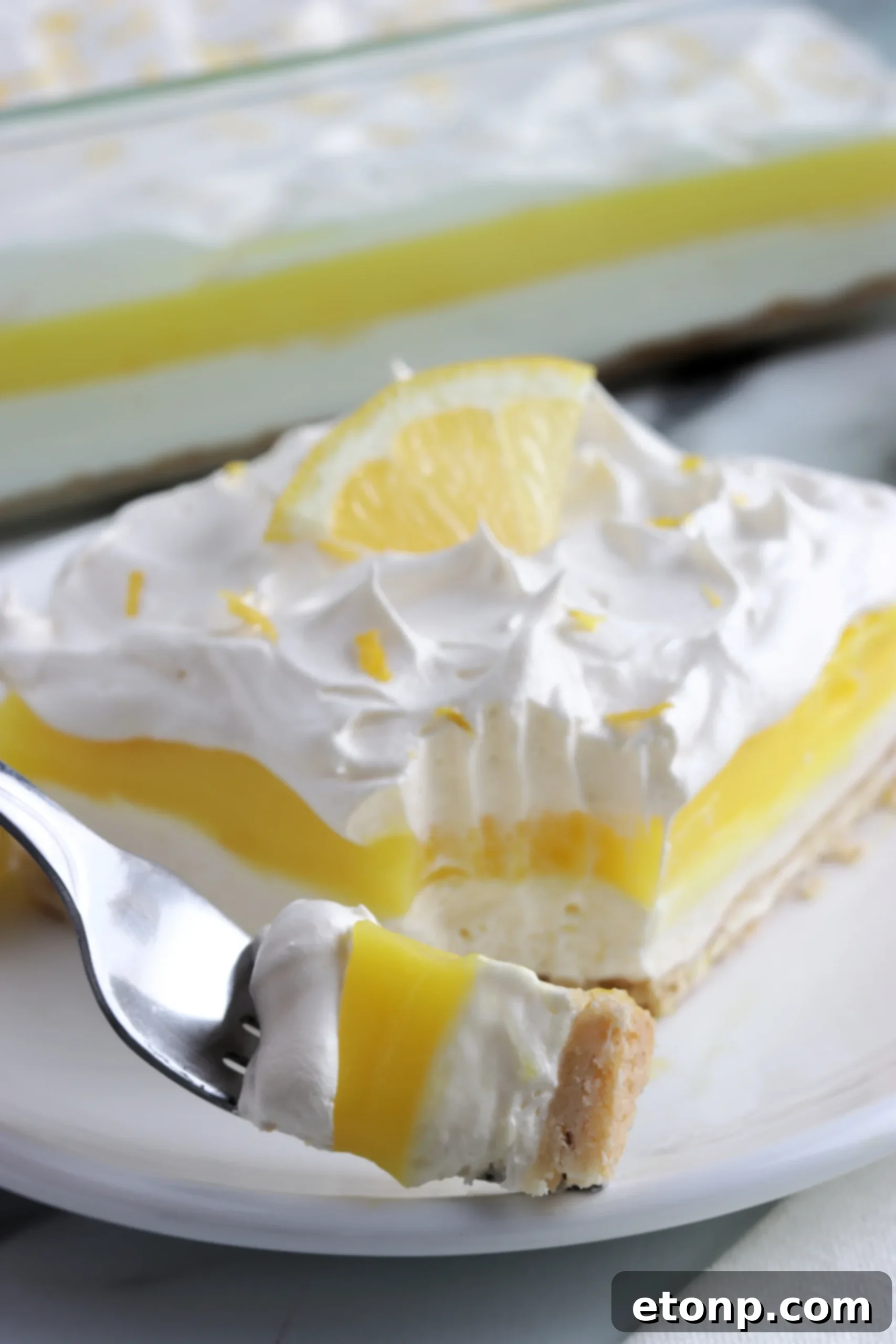 Close-up of a slice of Lemon Lush Dessert with layers clearly visible and a lemon wedge garnish.