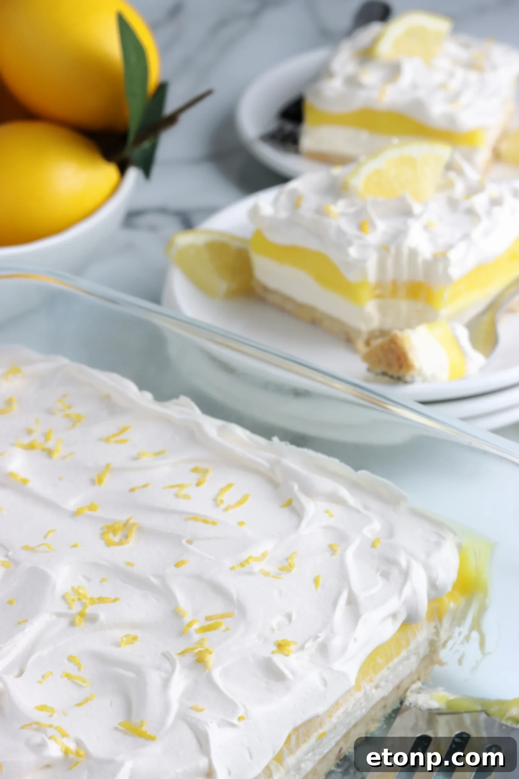 A serving spoon lifting a generous portion of Lemon Lush Dessert from a glass baking dish, showing all the creamy layers.