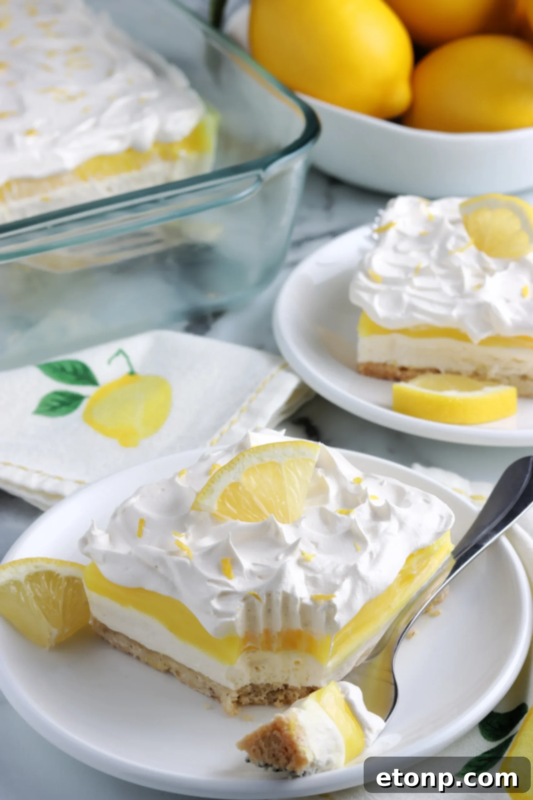 A close-up of a single slice of Lemon Lush Dessert on a white plate, revealing the golden crust, white cream cheese layer, yellow pudding, and white whipped topping.