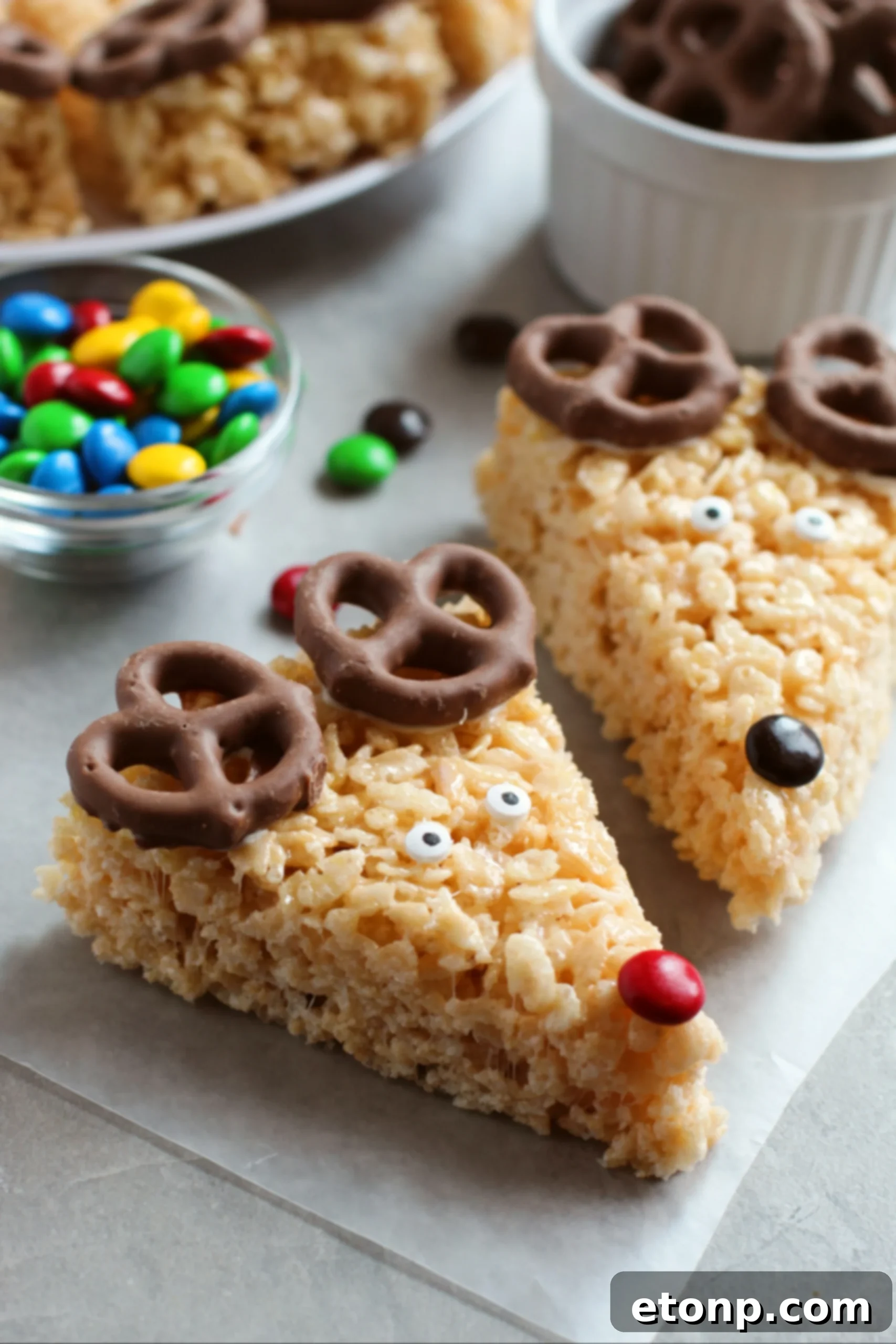 A close-up of several Reindeer Rice Krispie Treats, showcasing their chocolate pretzel antlers, candy eyes, and M&M noses.