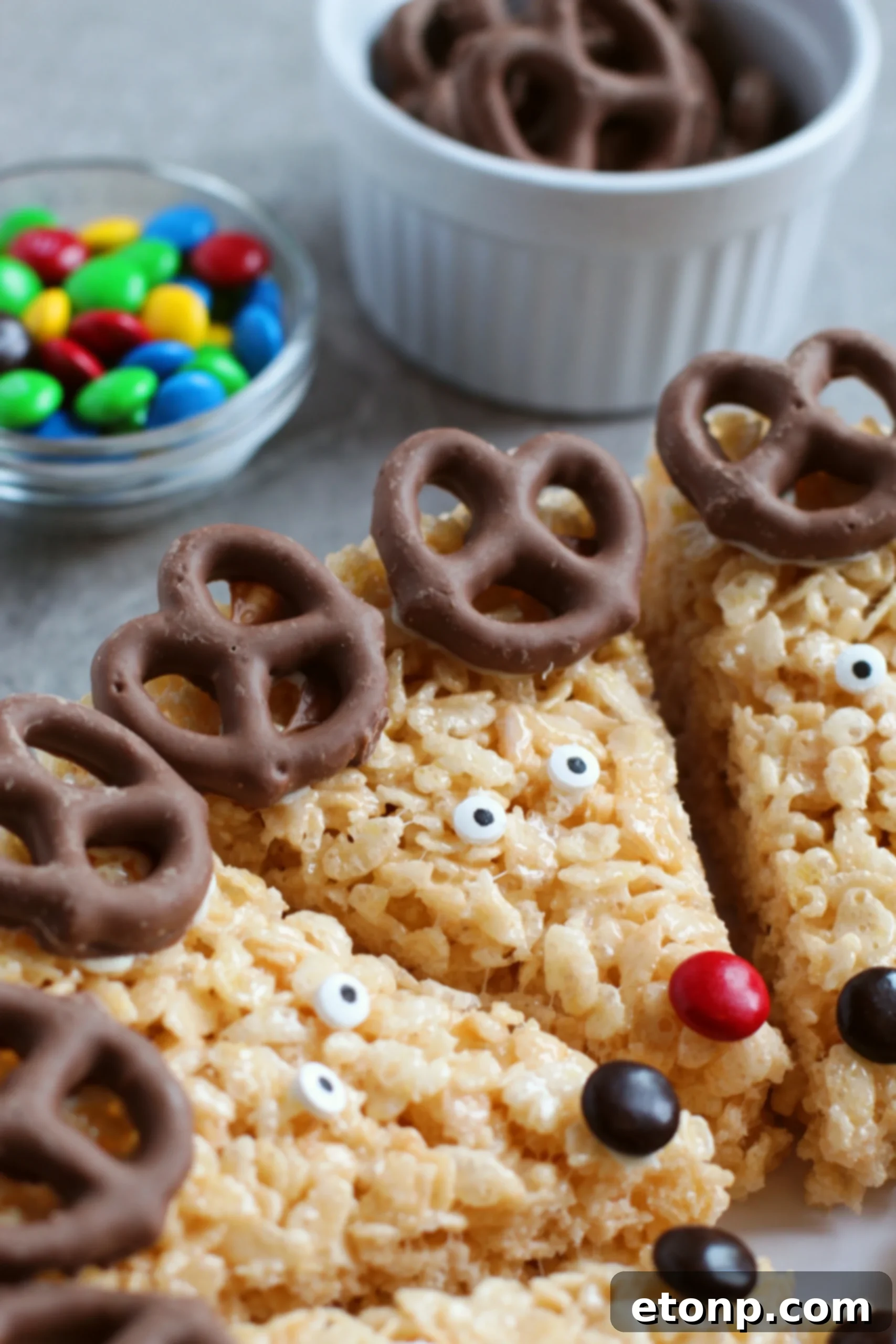 Individual ingredients for Reindeer Rice Krispie Treats: mini marshmallows, chocolate covered pretzels, candy eyes, and M&Ms.