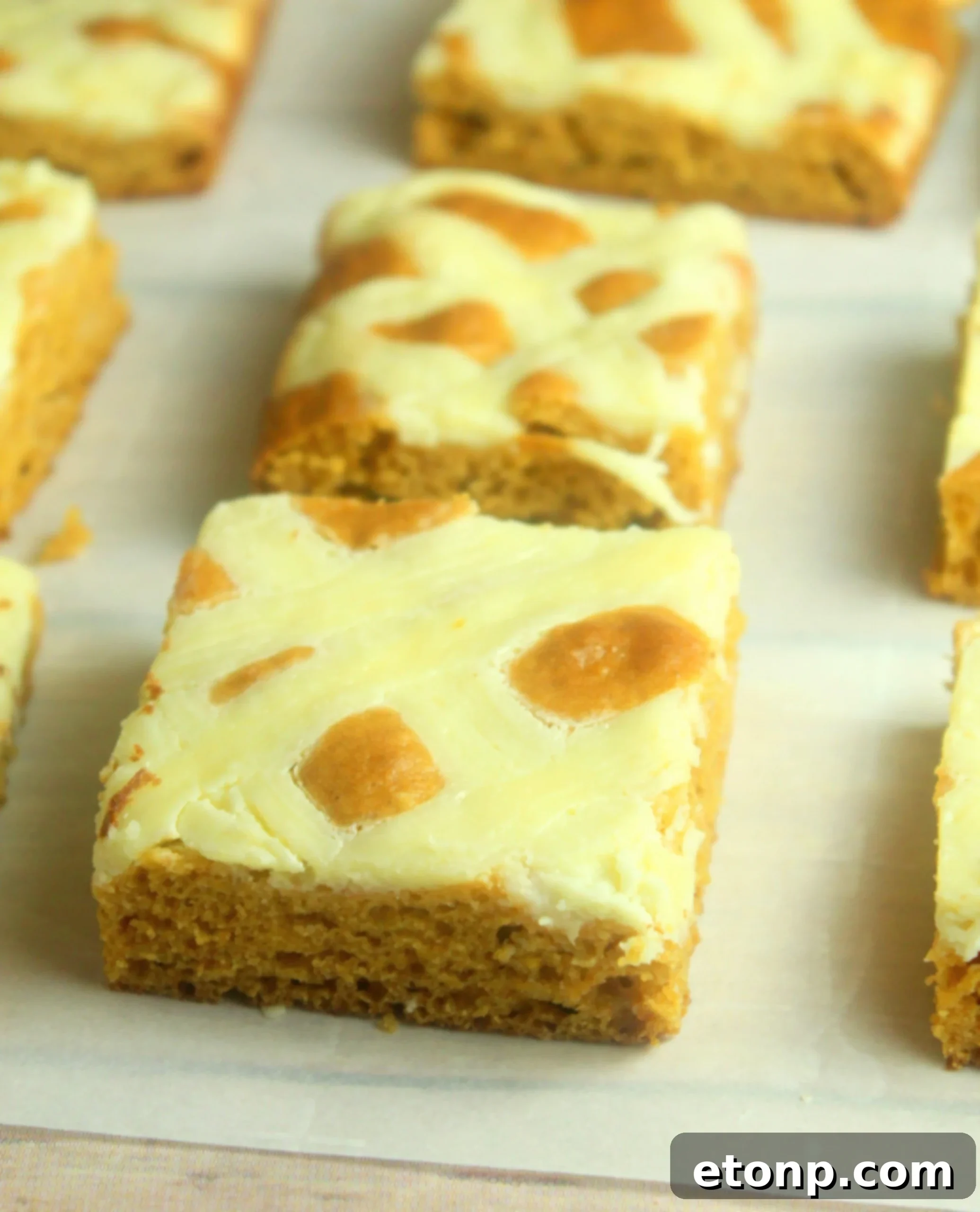 A stack of freshly baked and cooled Extreme Cream Cheese Pumpkin Bars on a rustic wooden board, ready for slicing.