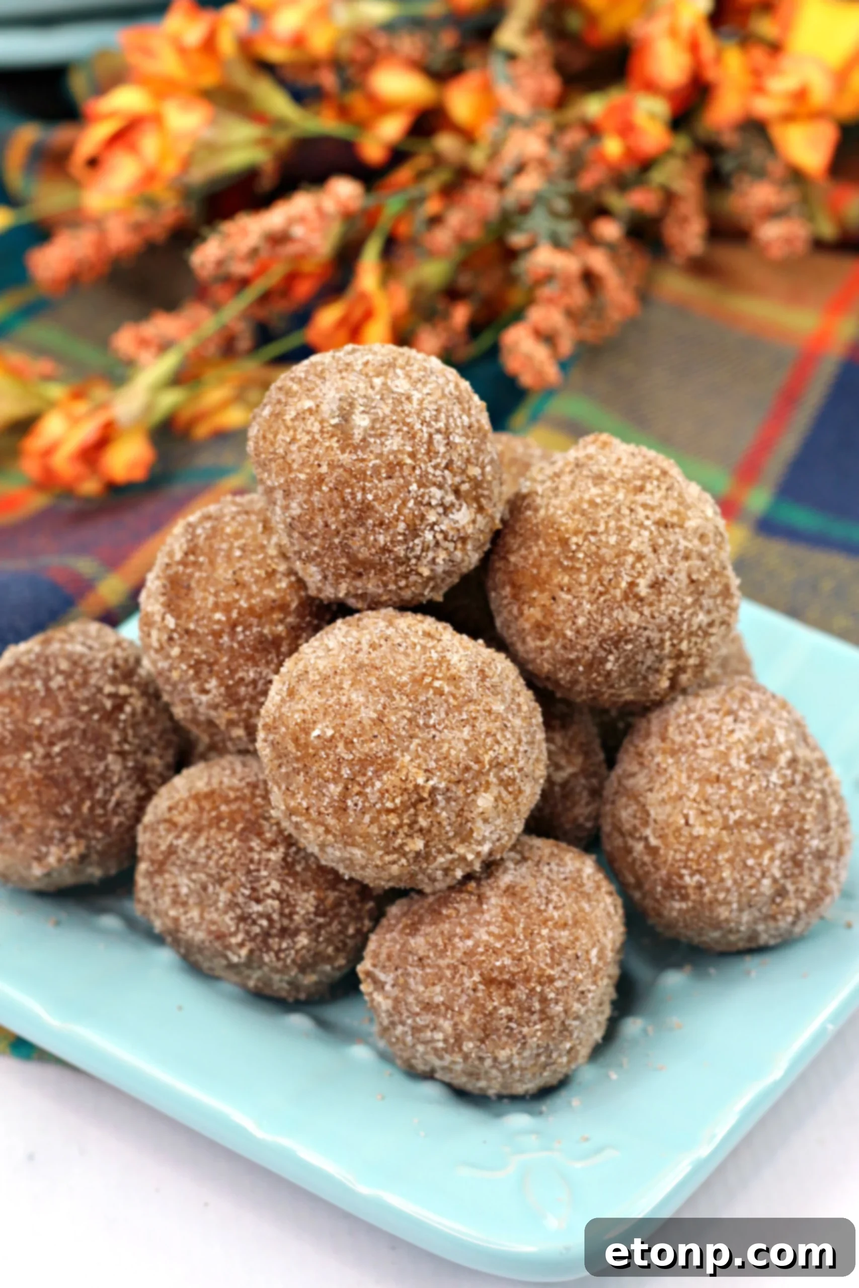 A hand reaching for a Pumpkin Snickerdoodle Donut Hole from a tray