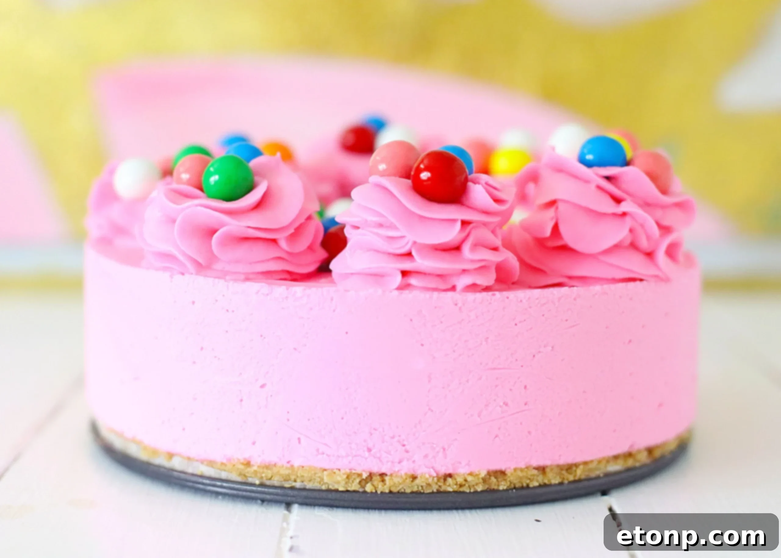 A hand gently folding colorful gumballs into the pink cheesecake batter.