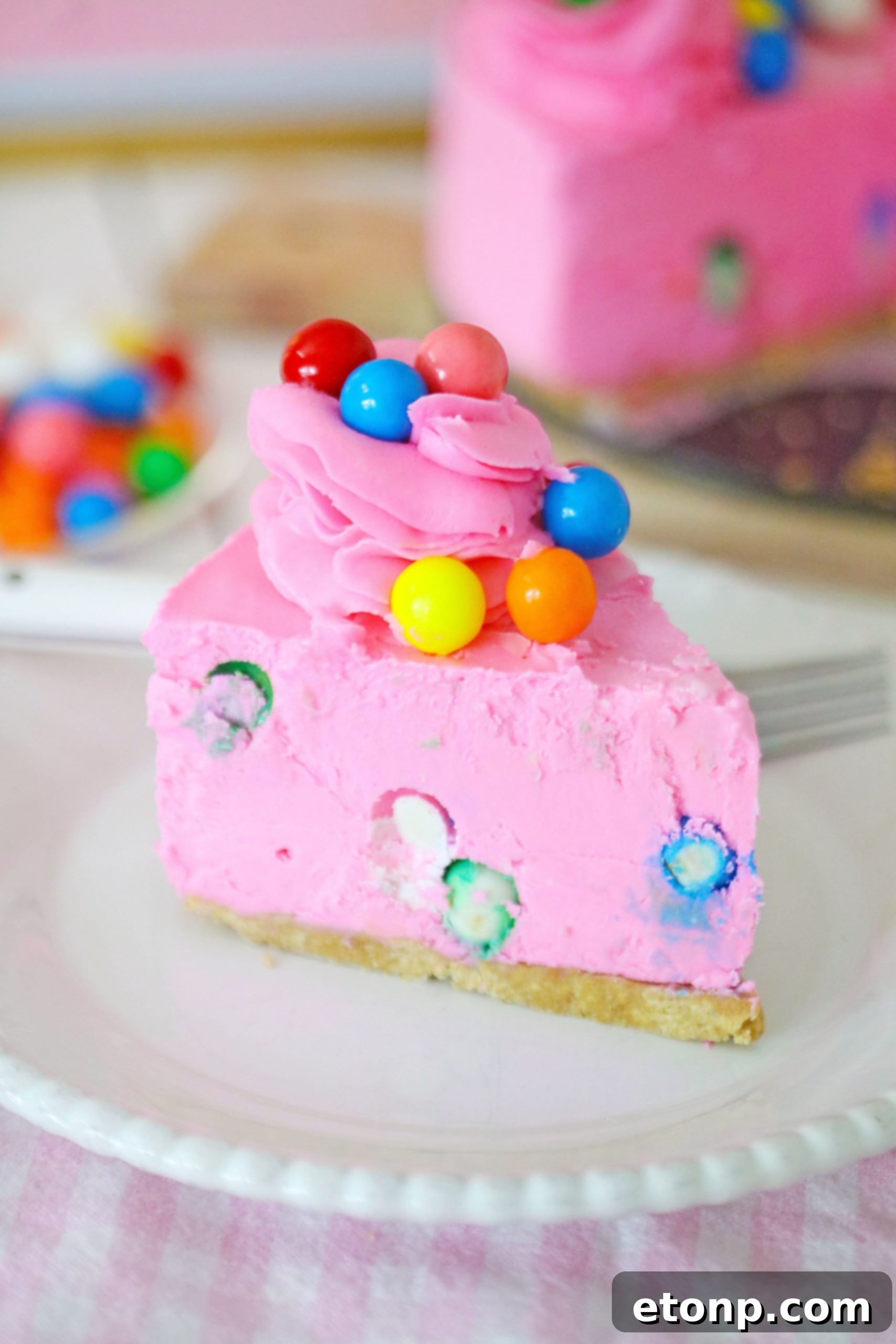 A beautifully decorated pink bubblegum cheesecake with frosting swirls and gumballs on top, perfect for a birthday.