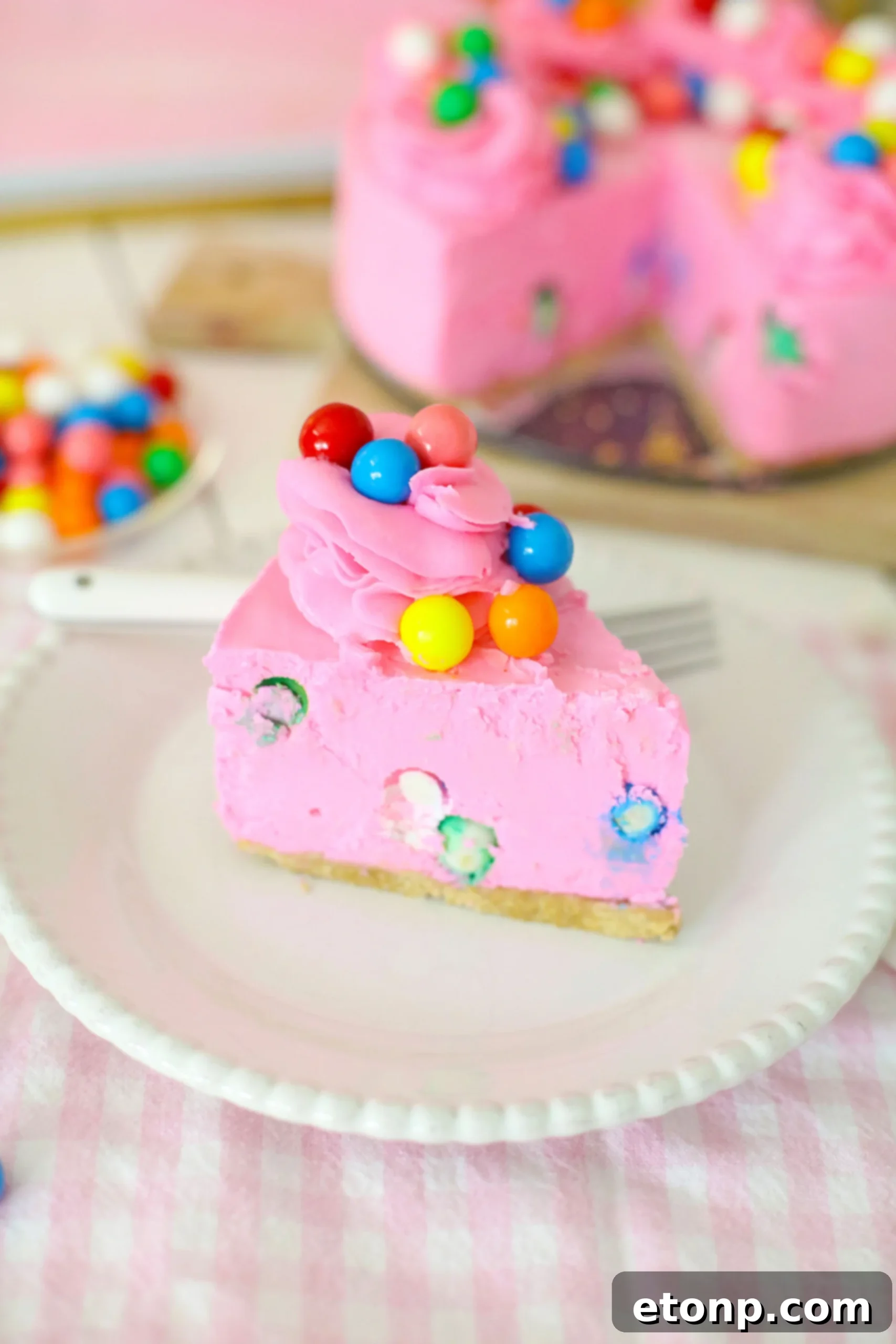 A close-up shot of a slice of Bubblegum Cheesecake with visible gumballs, showcasing its appealing texture and color.