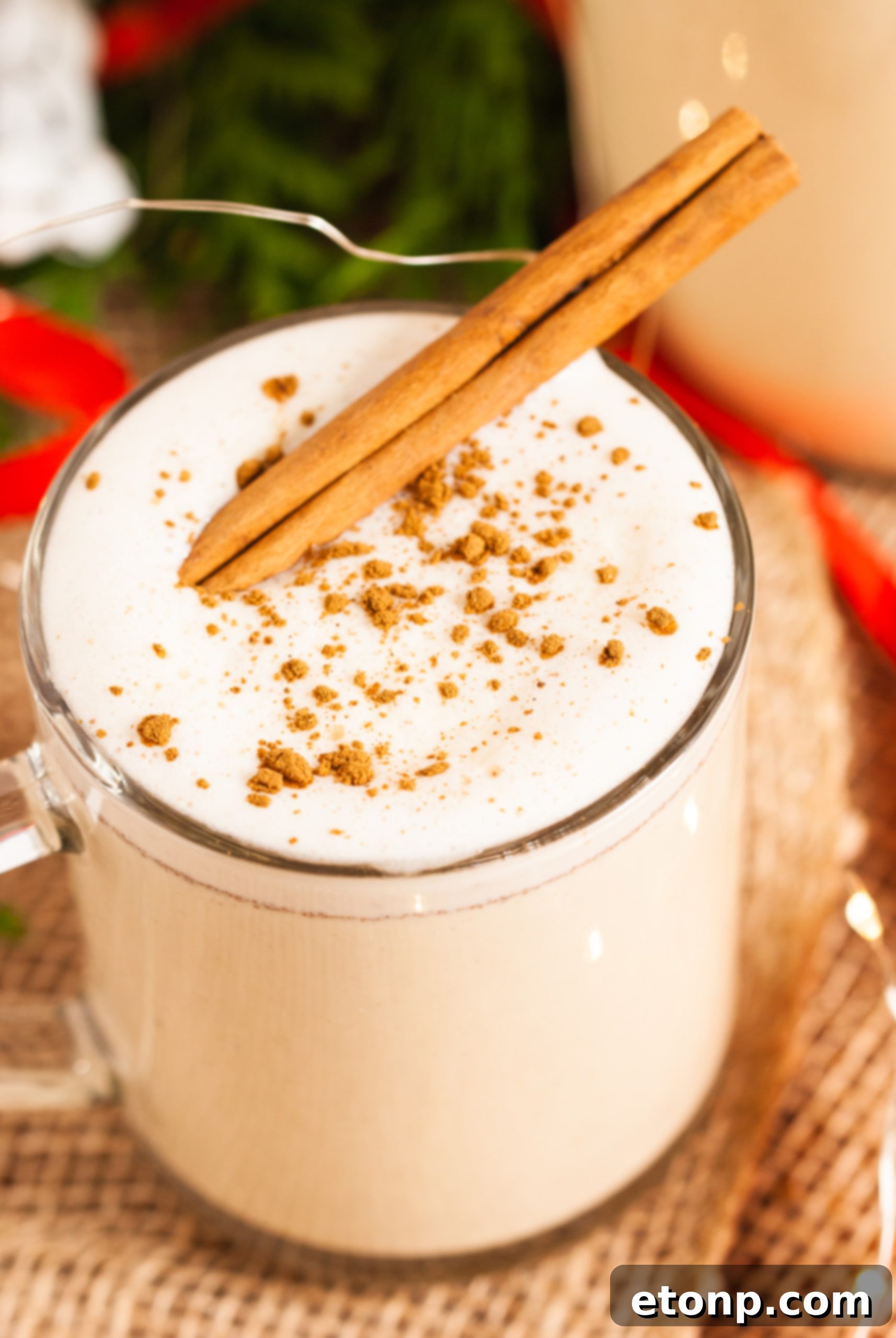 Overhead view of a prepared glass of eggnog with whipped cream and a cinnamon stick, accompanied by whole spices.