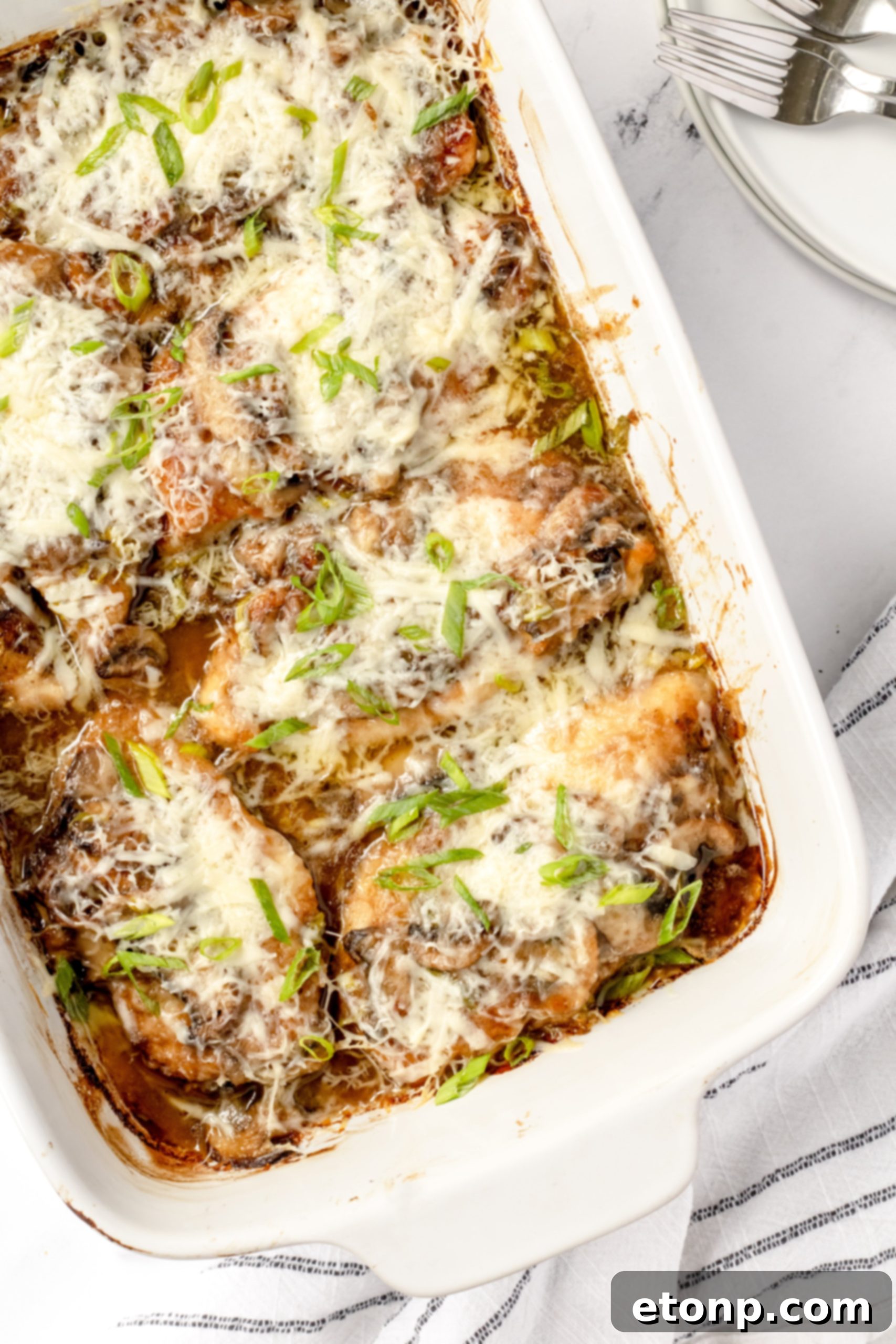 A beautifully plated dish of Chicken Lombardy, featuring golden-brown chicken cutlets topped with creamy mushroom Marsala sauce, melted Parmesan cheese, and fresh green onions, served with a garnish of parsley.