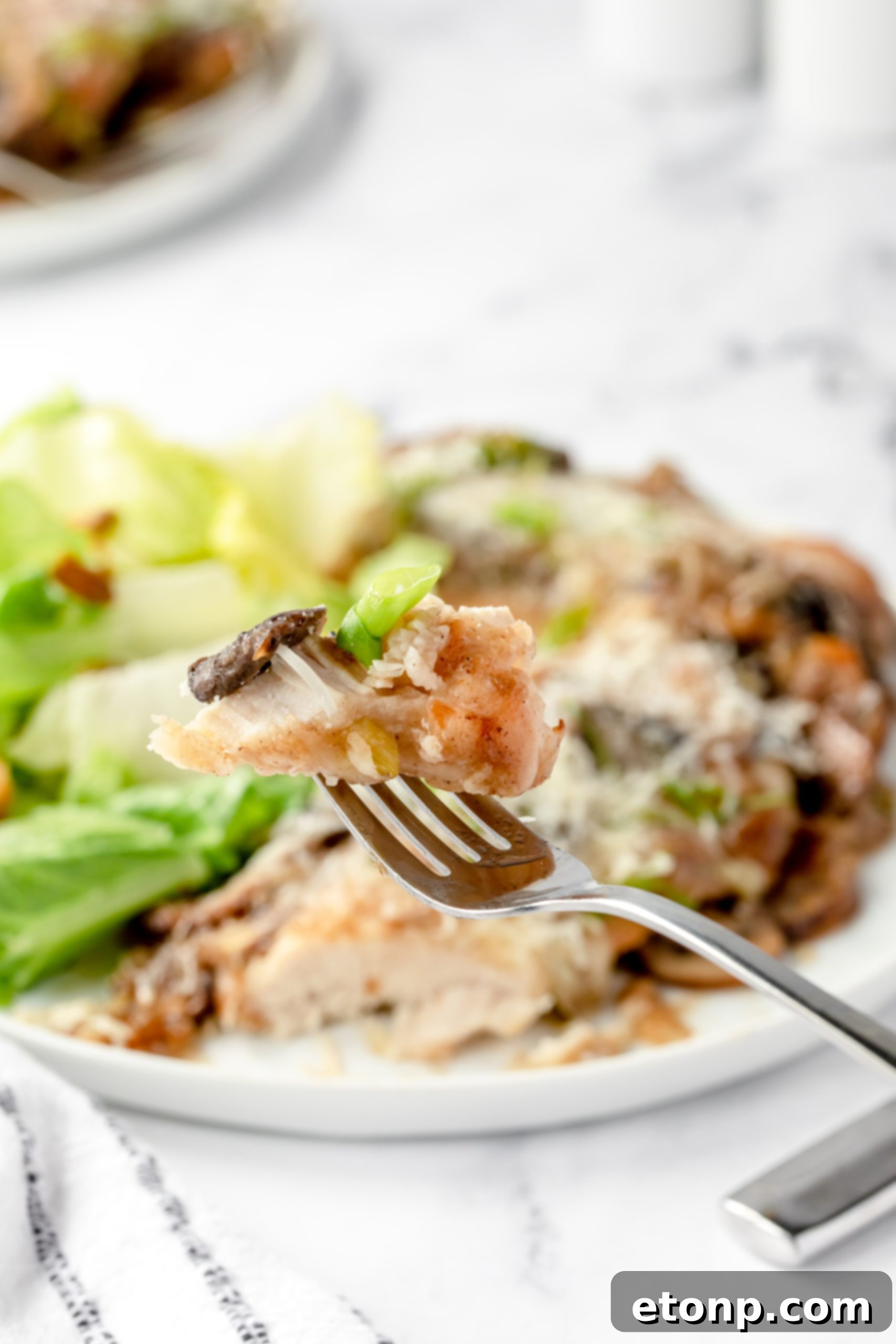 A cook's hand, holding a spatula, placing seared chicken cutlets into a baking dish, preparing for the next step of layering with sauce and cheese.