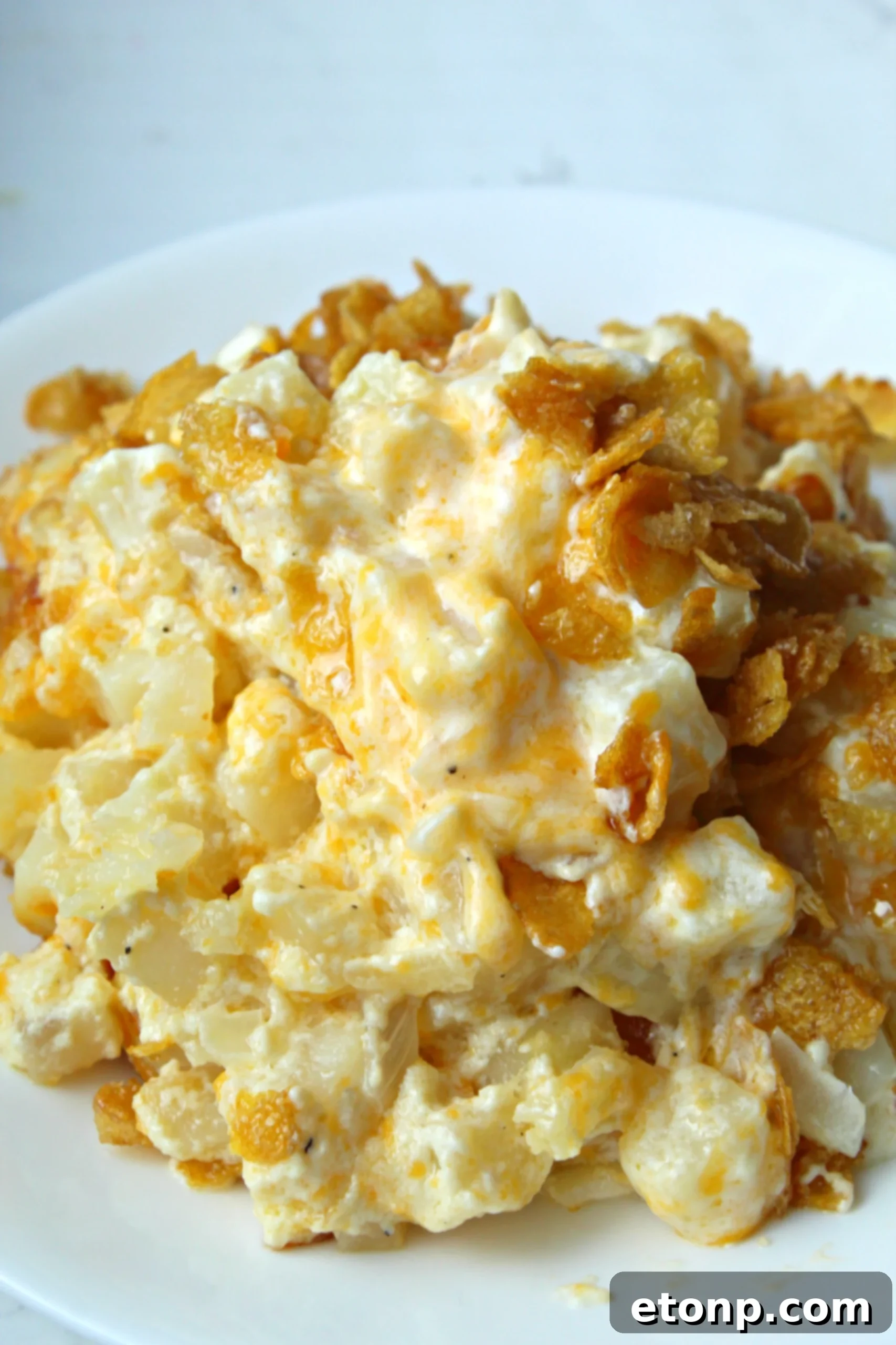 A dish of Funeral Potatoes with a golden, buttery cornflake topping being prepared.