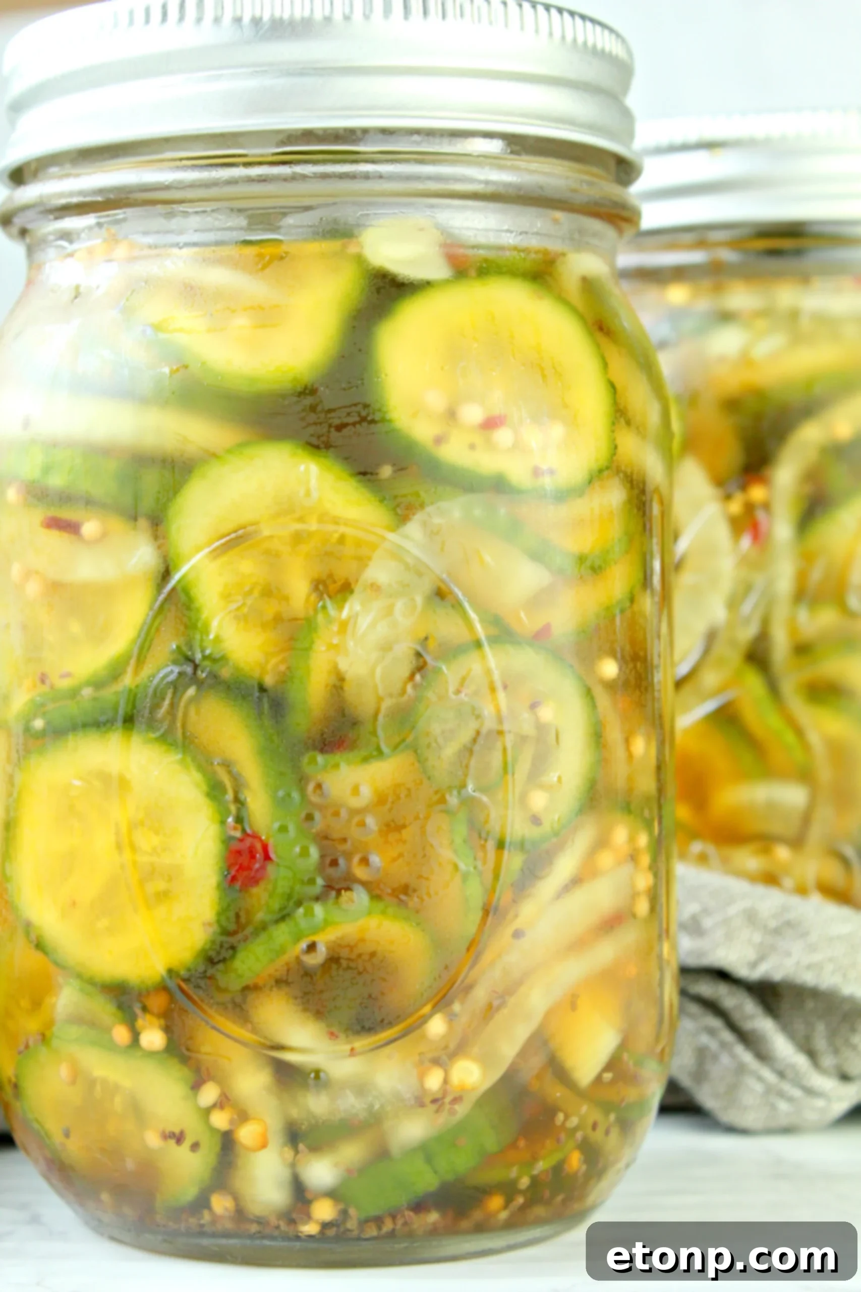 A large glass jar filled with vibrant yellow and green homemade bread and butter pickles, sealed and ready for refrigeration.